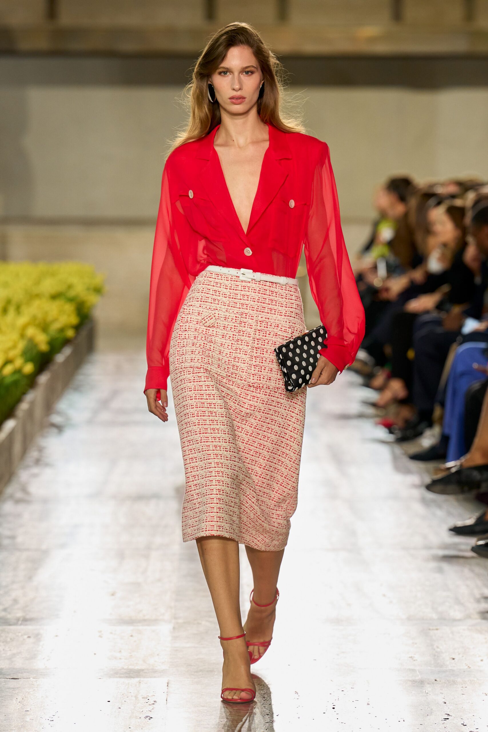 Sheer scarlet chiffon blouse with a plunging lapel front and flap pockets. Cream pencil skirt in nubby boucle, cinched with a slim white belt. Black clutch dotted in white spots. Red ankle-strap sandals with bare, narrow toe bands. Silver hoop earrings. Walking into a hotel lunch where the terrace tables are already taken.