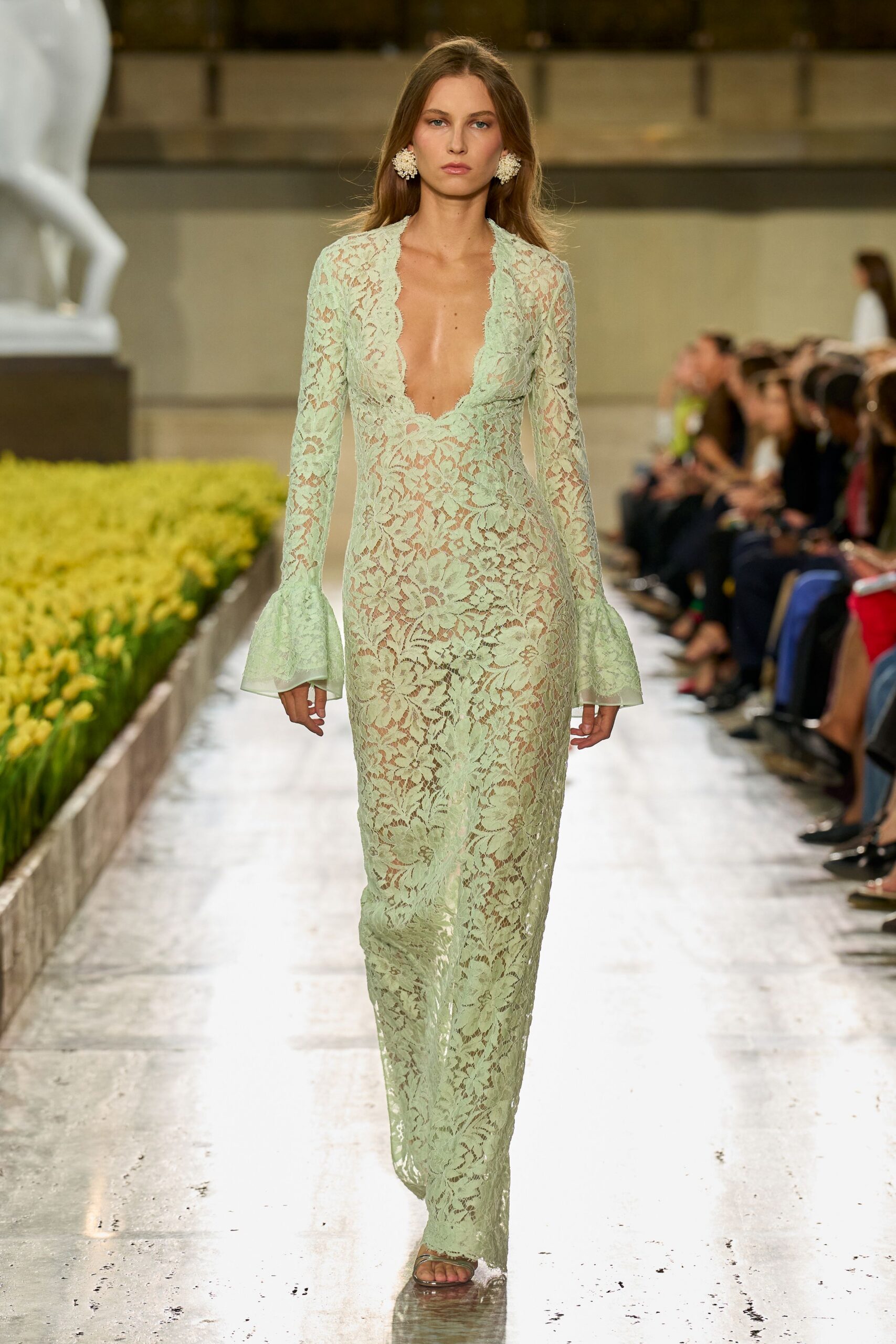 Cluster earrings like white blossom pinned close to the lobe. Mint floral lace column dress, plunging scalloped neckline and fluted cuffs. Barely there straps under a lace-skimming hem. Crossing a conservatory aisle while the irrigation has just clicked on.