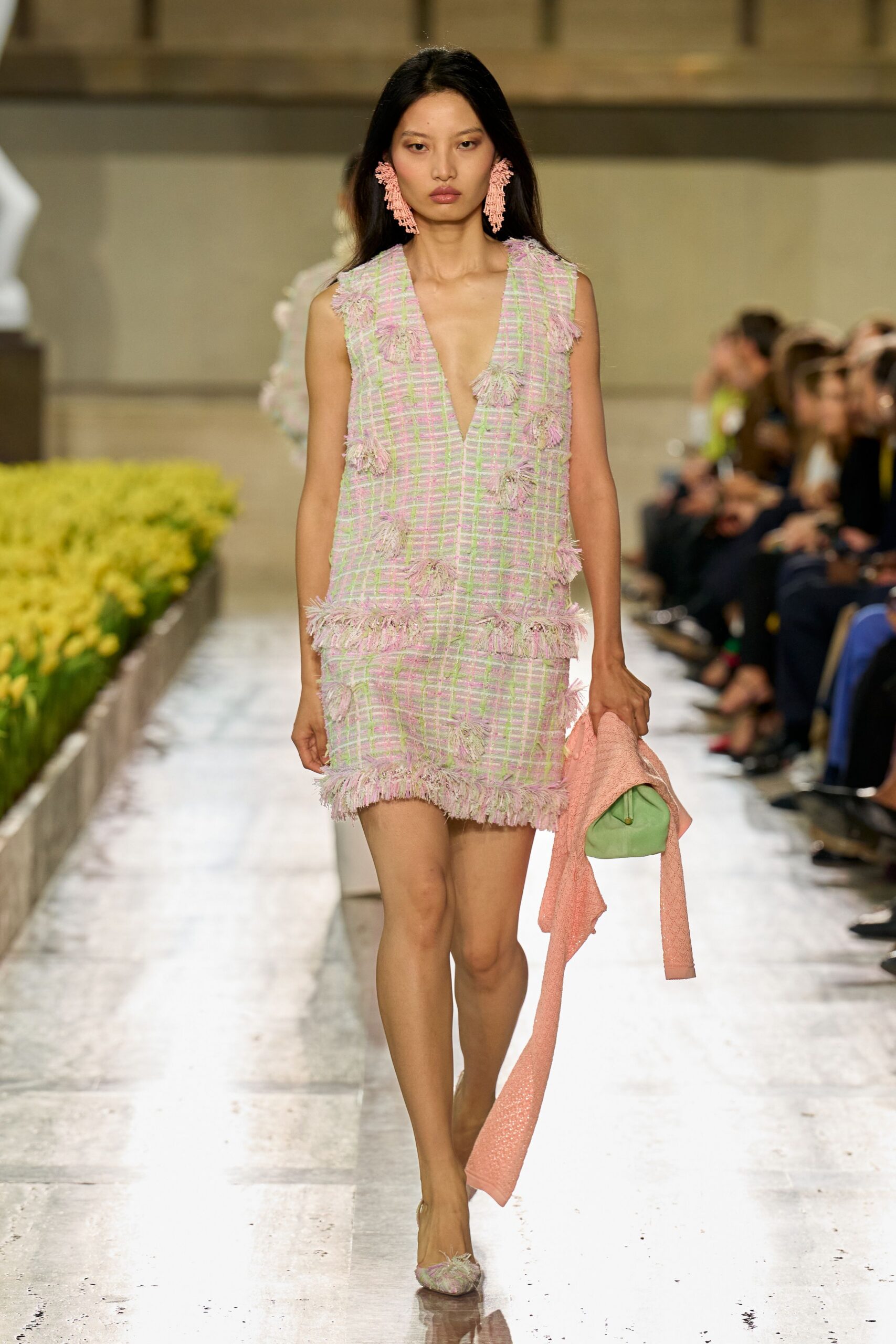 Pink beaded chandelier earrings brushing the jaw. Pastel plaid tweed shift, deep plunge and fuzzy fringe tufts. Peach bouclé knit carried loose from one hand. Mint pouch bag with a rounded frame. Pointed flats topped with matching tweed fringe. Easter brunch on a hotel terrace before the sun turns sharp.