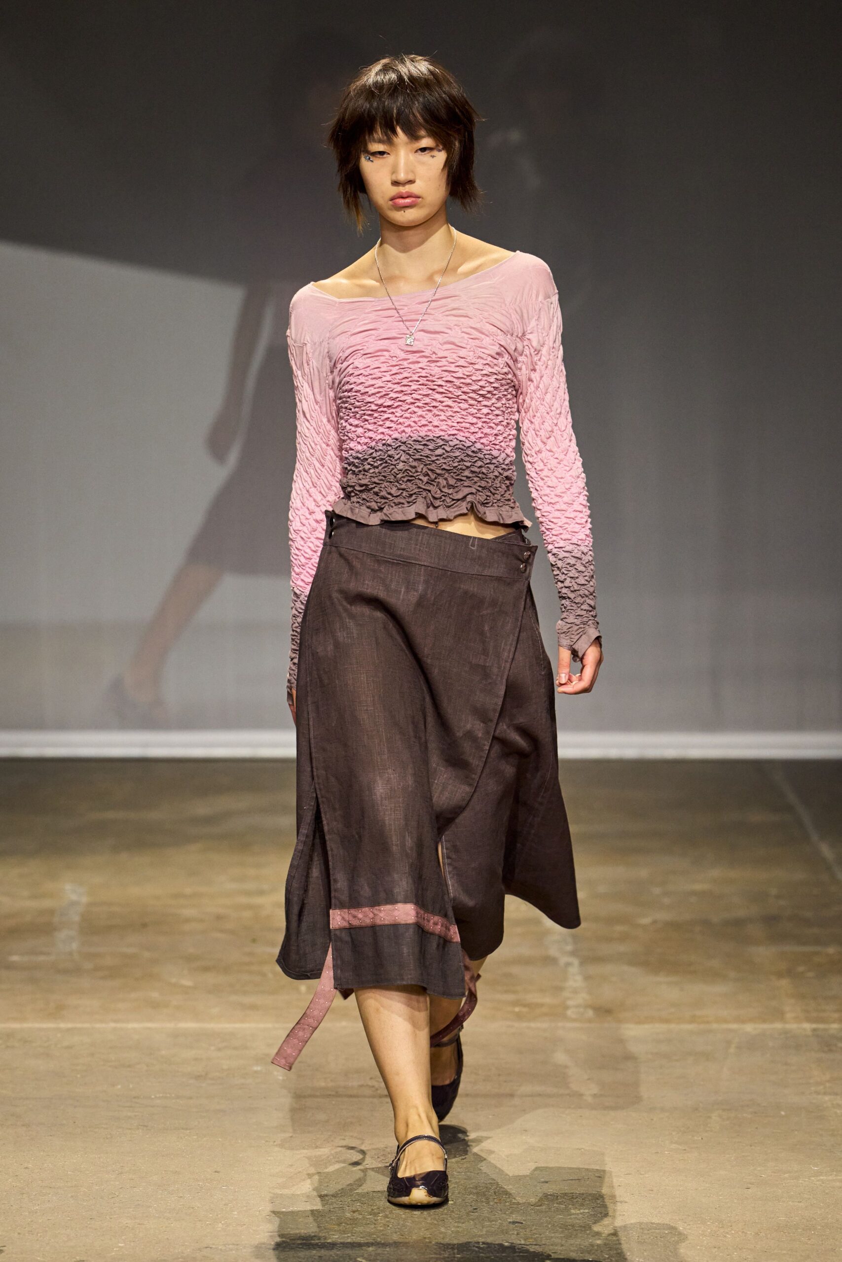 Pink-to-mauve ruched top, crinkled tight through the torso and sleeves. Smoke-brown wrap skirt in slubby weave, side slit and loose pink strap. Dark mary janes, toe cap worn pale. Fine chain with a tiny square pendant. Walking home with bakery paper still warm under your arm.