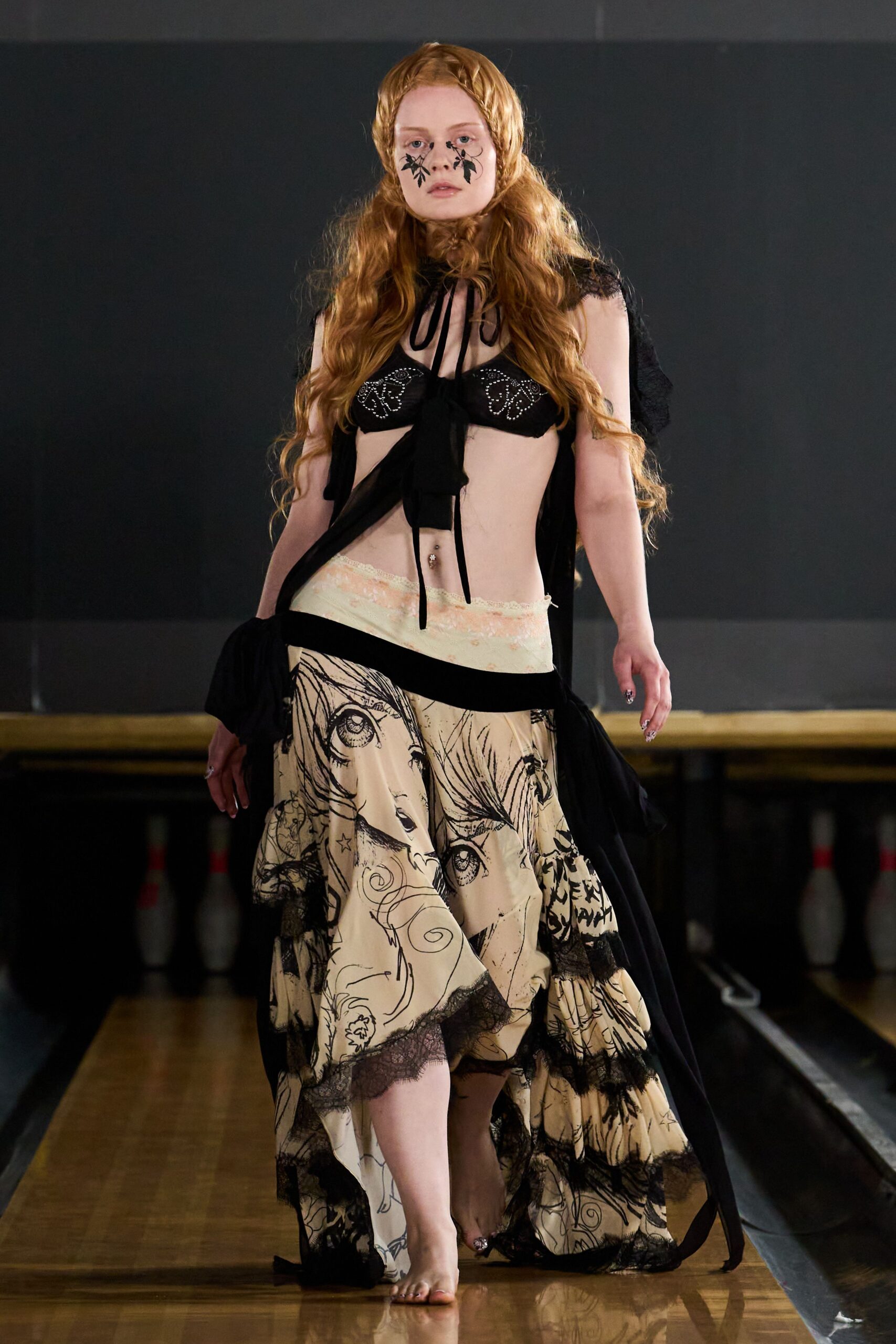 Black leaf shapes pasted beneath both eyes. Black bra cups dotted with rhinestone butterfly outlines. Sheer black capelet tied at the throat with long cords. Cream drop-waist skirt printed with manga faces, black lace at the tiers. Walking barefoot down a bowling alley after the league has gone home.