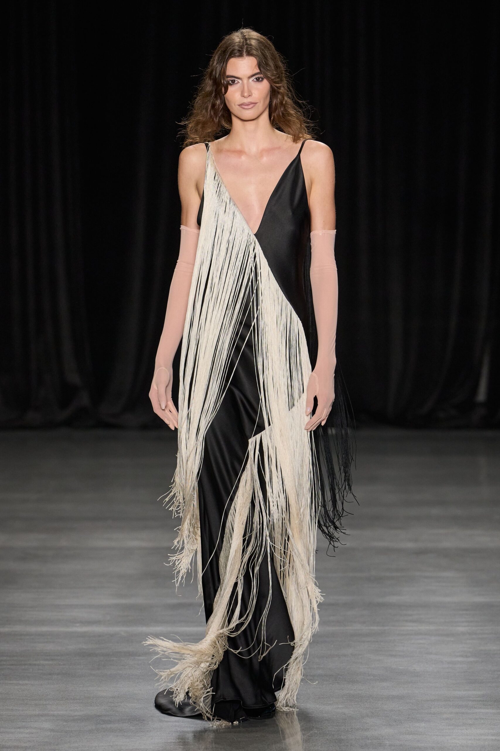 Black satin slip gown split by sweeping panels of cream and black fringe. Pale blush mesh opera gloves, ending just above the bicep. Black satin boots, square at the toe. Whatever you wear when the hotel bar pianist keeps playing after midnight.