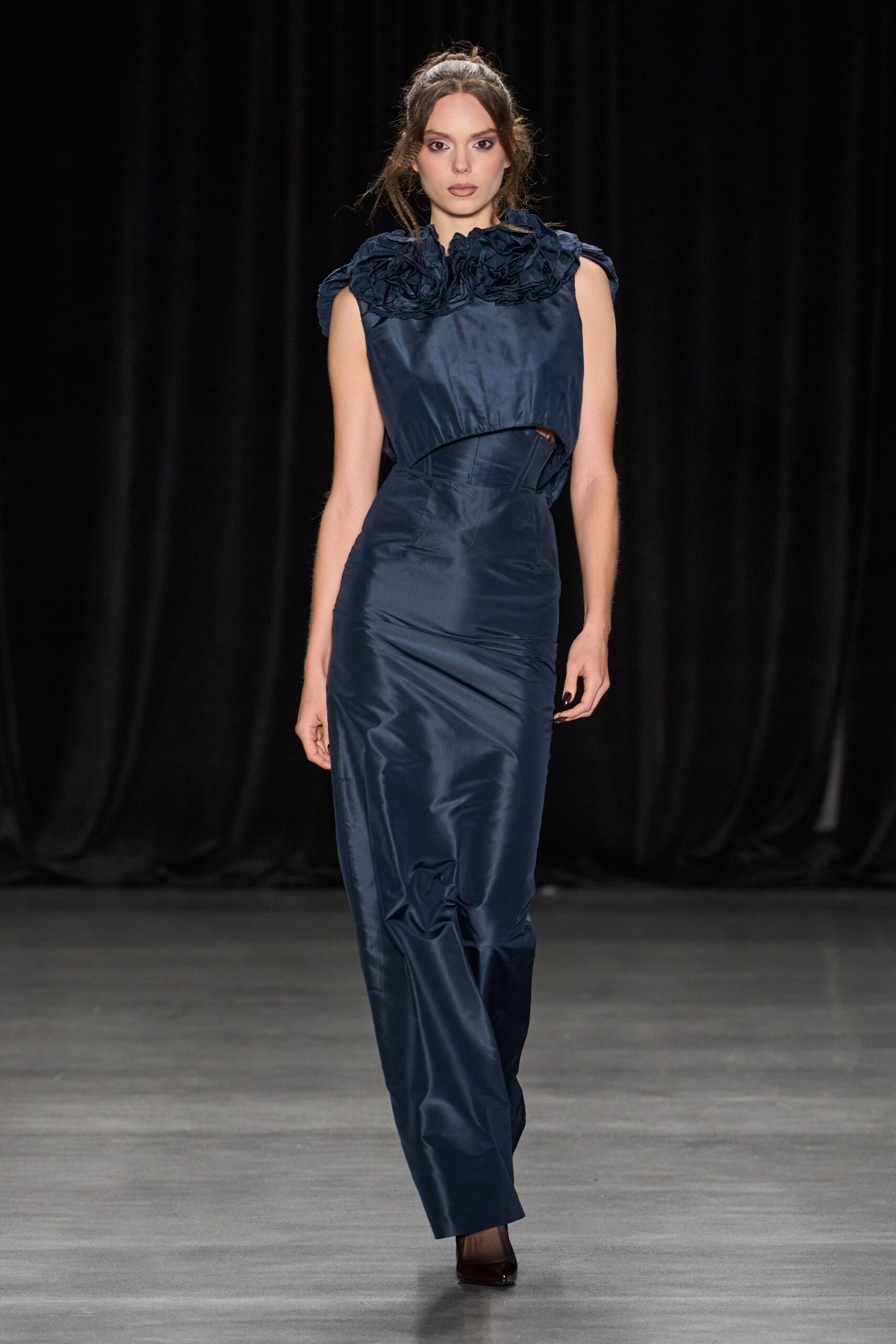 Midnight taffeta shell with crushed rosettes crowding the neckline. Matching underbust corset, curved seam panels peeking through the waist cutout. Column skirt in the same sheen, wrinkling softly through the shin. Dark patent pumps. For arriving at the benefit after taking off a wool coat in the car.