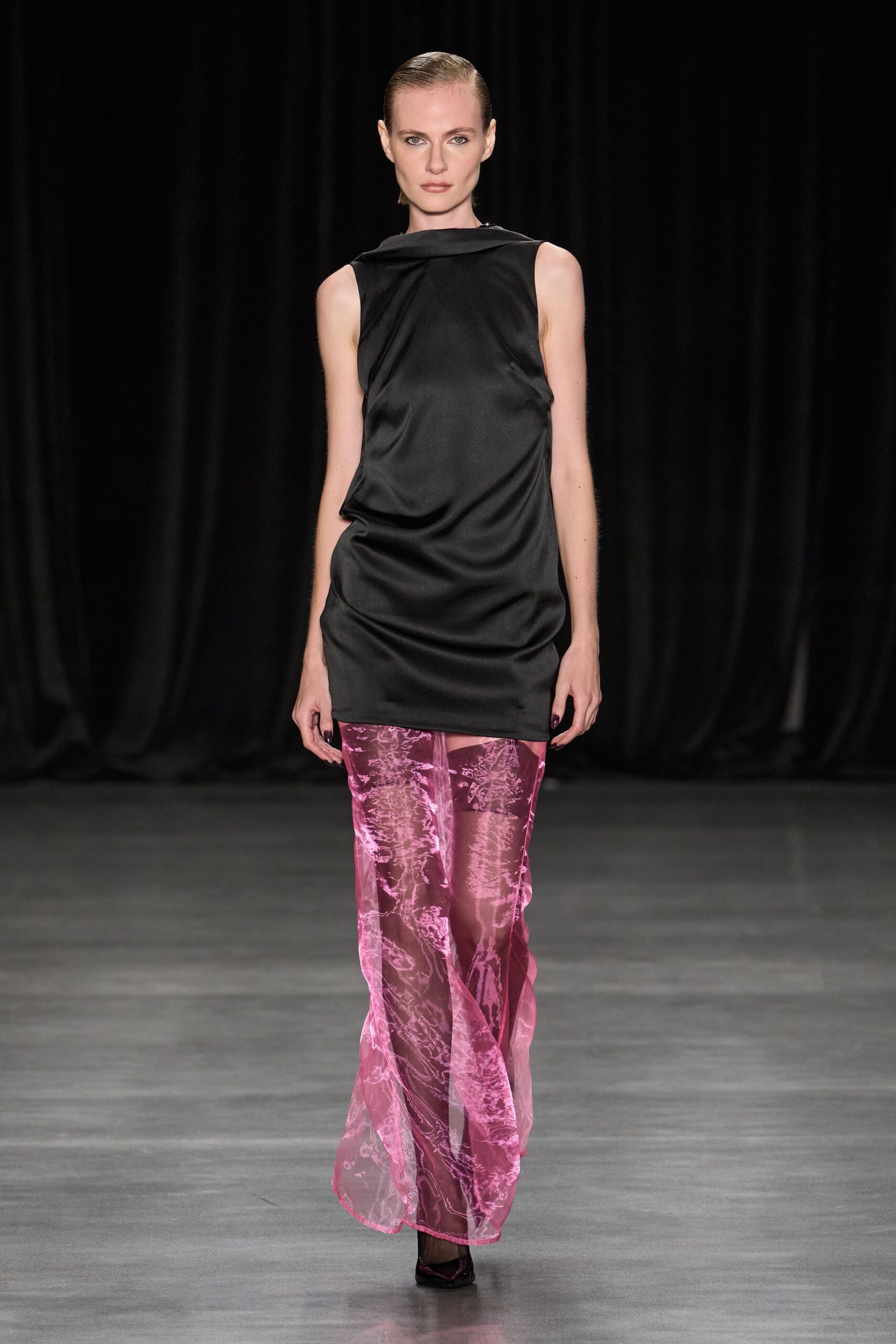 Black satin tunic dress, cut with a folded boatneck and slumped drape. Sheer rose organza trousers, marbled burnout swirling over the legs. Pointed dark pumps, barely visible under the hem. Whatever you wear to read tarot in a hotel bar before noon.