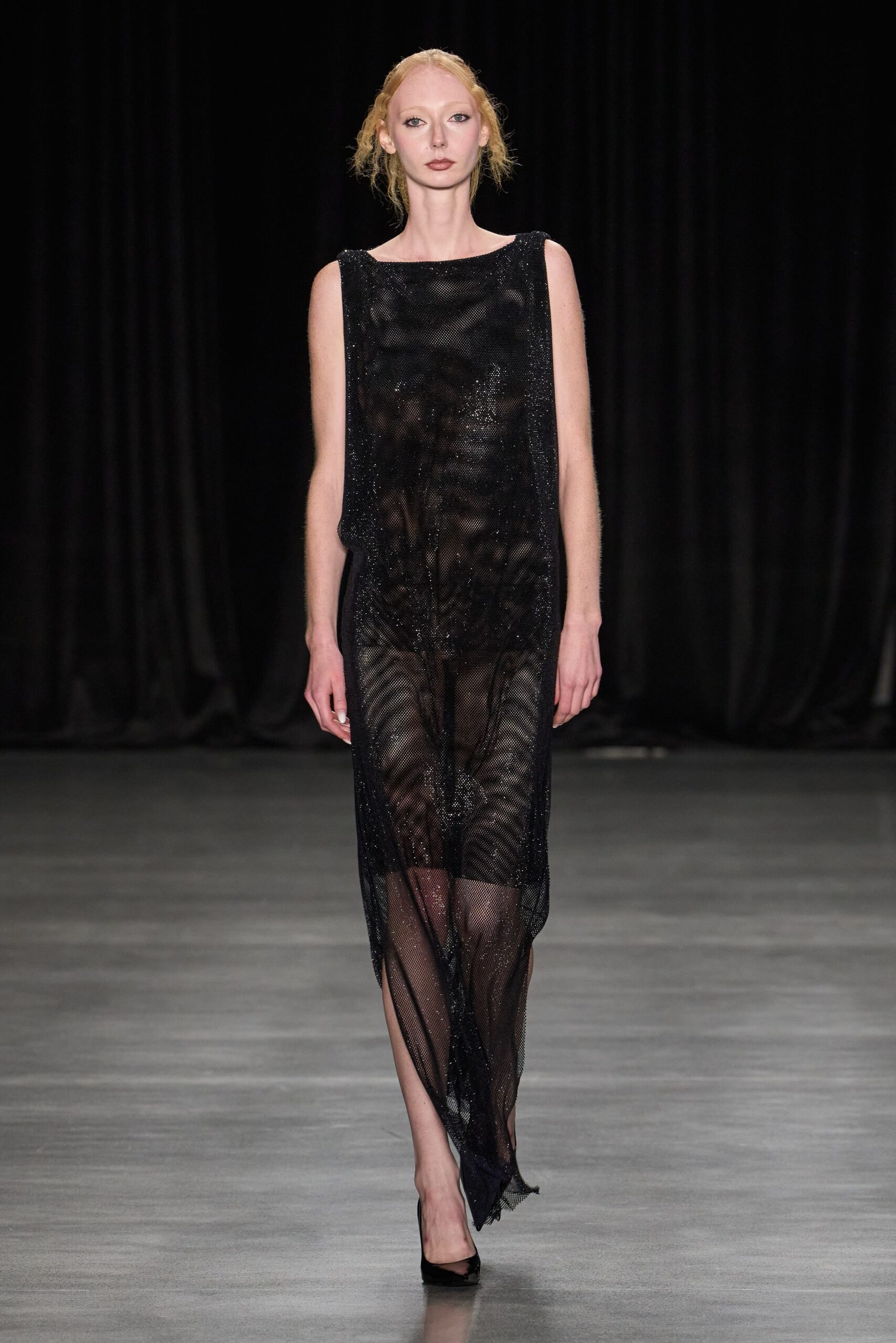 Black glitter-mesh column dress, boatneck and zebra-shadowed sheer panels. Black patent pumps, sharply pointed. After midnight at the aquarium, only the tanks still lit.