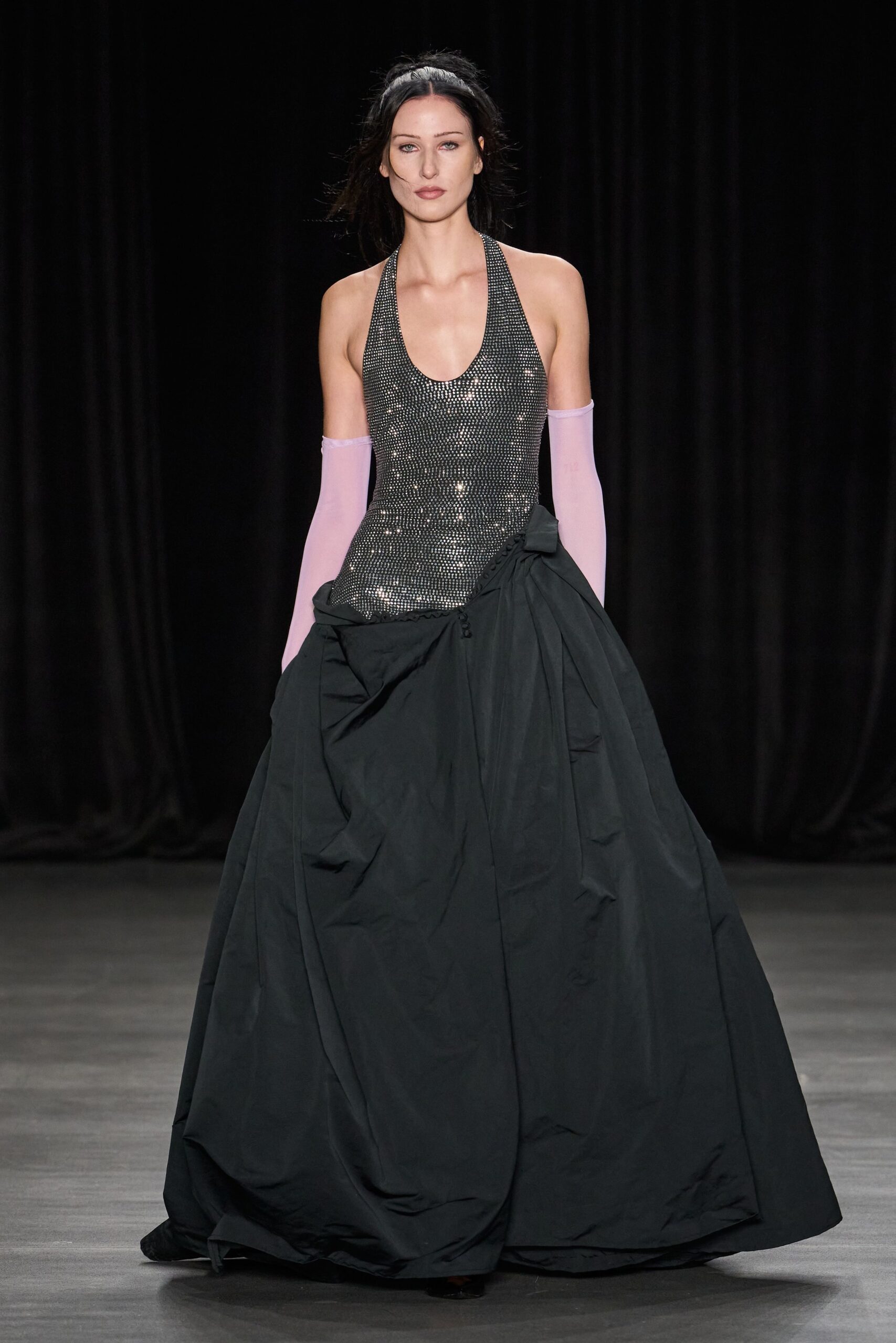 Gunmetal micro-sequins packed tight over a deep scoop halter bodice. Pale lilac sheer gloves ending in a soft rolled edge. Black taffeta overskirt ballooning from the hips, ruched with tiny covered buttons. Whatever you wear home after midnight fireworks and a torn party tent.