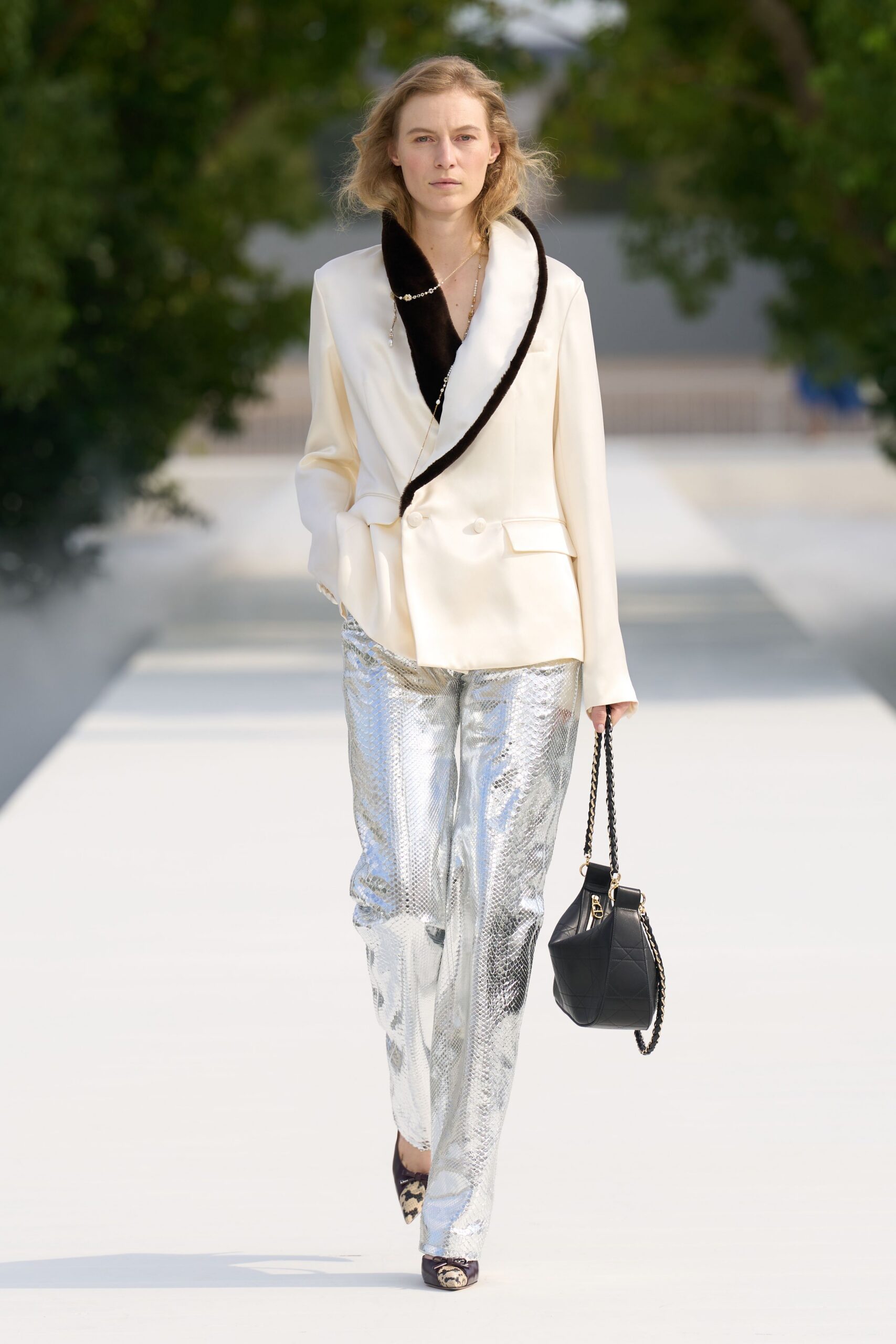 Cream double-breasted blazer with a deep black velvet shawl collar. Long pearl strand looping loosely across the lapel. Silver python trousers, liquid shine broken by soft creases. Black cannage bucket bag on a chain strap. Leopard-toe pumps with tiny bow ties. Walking garden paths after lunch, still dressed for the table.