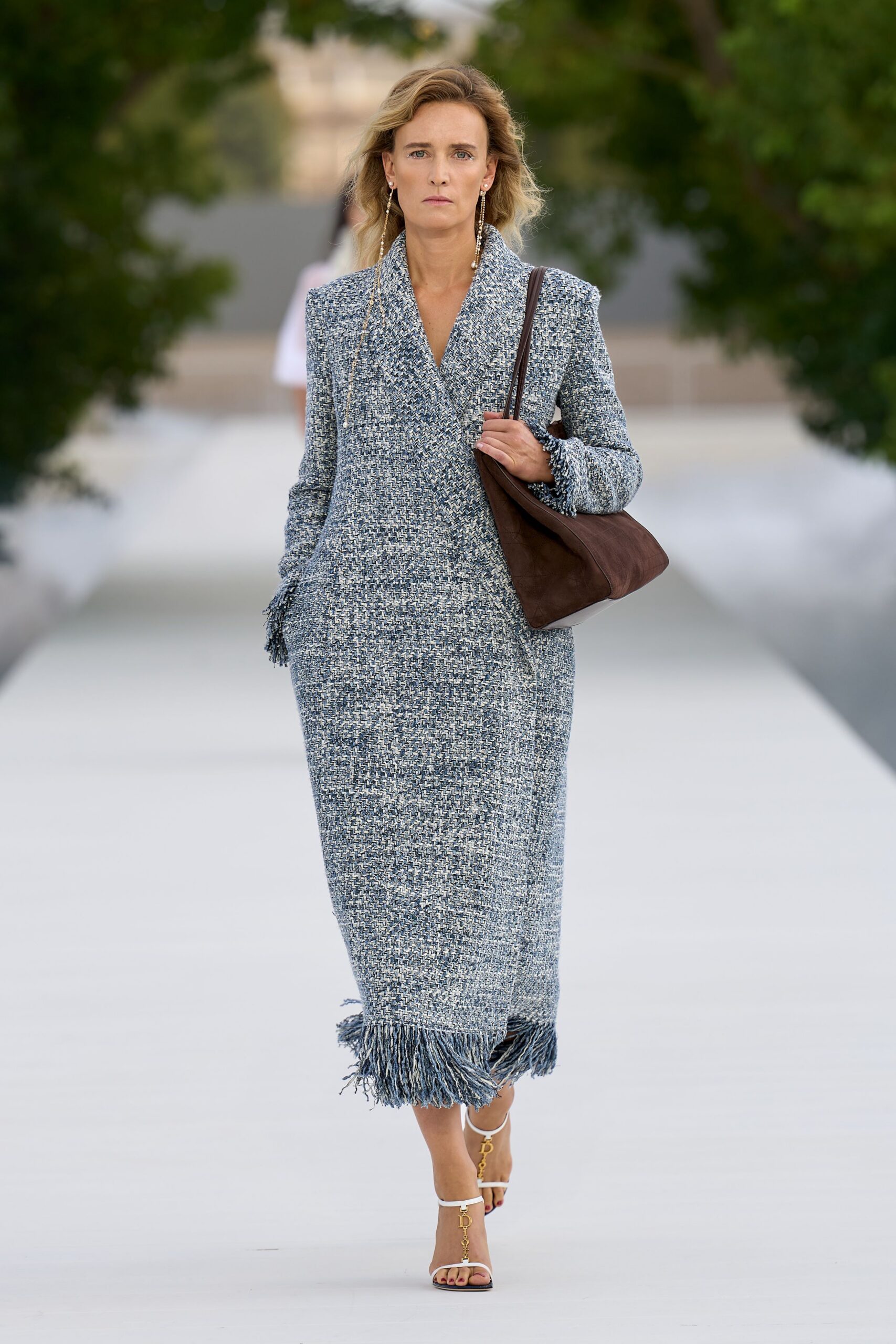 Blue-and-ivory basket-weave column dress with fringed cuffs and hem. Slouchy brown leather tucked close under the arm. White thong heels with dangling gold letter charms. Crossing a hotel courtyard before noon, room key still warm in hand.