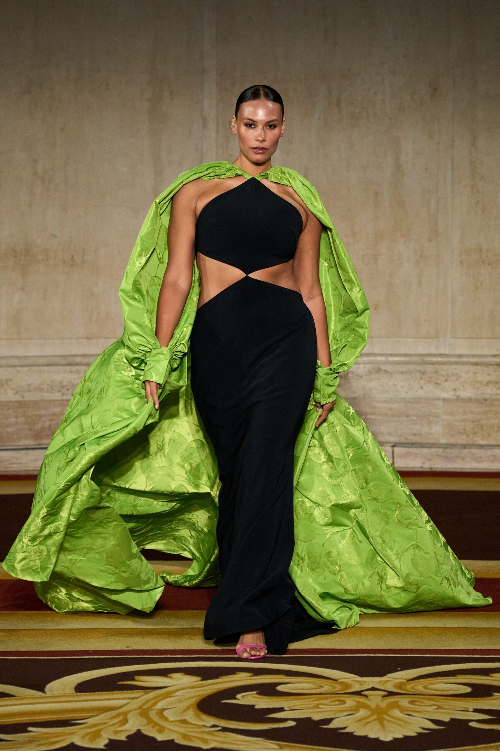 Acid-lime floral jacquard opera coat, bunched into cuffs and dragging behind. Black halter gown with a pinched waist cutout and fluid floor-length skirt. Hot-pink thong sandals peeking out under the hem. Crossing a hotel ballroom carpet after everyone else has gone upstairs.