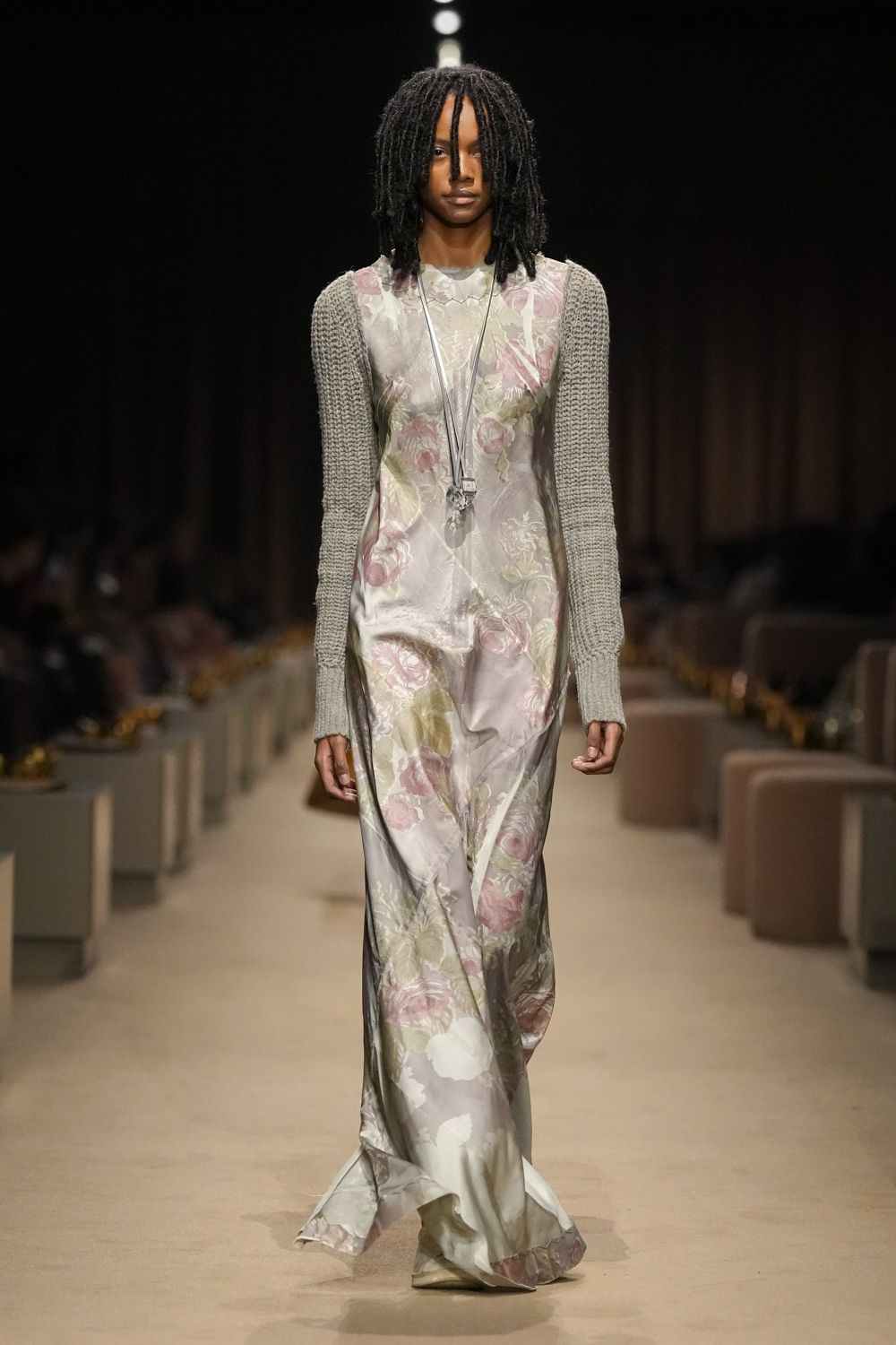 Floor-length satin slip dress washed with blurred peony roses. Long oatmeal knit sleeves, chunky and detached from the dress. Clear crystal pendant hanging low on doubled cord. Pointed shoes veiled by the dragging hem. Hotel corridor at dawn, carrying your shoes after the wedding.