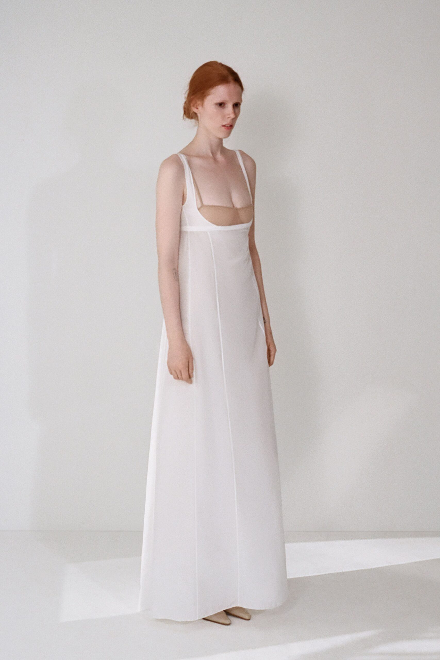 White column gown with a square cutout bodice and long vertical seaming. Pointed nude pumps barely peeking from the hem. Morning at city hall, holding the paperwork in both hands.