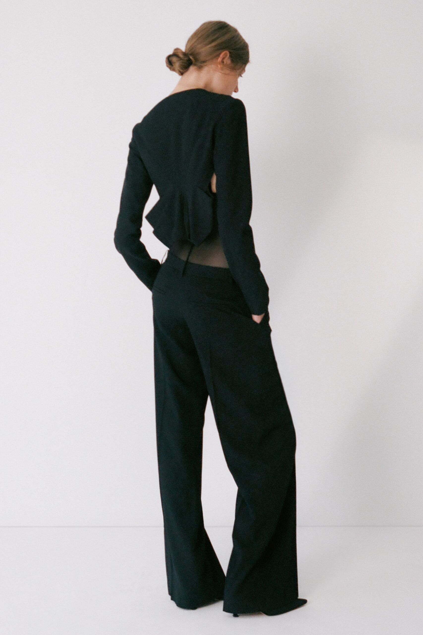 Black long-sleeve top cut open at the sides, peplum folded at back. Black wide-leg trousers with a sheer mesh waistband rising above the seat. For slipping out to the hotel corridor after everyone else has gone upstairs.