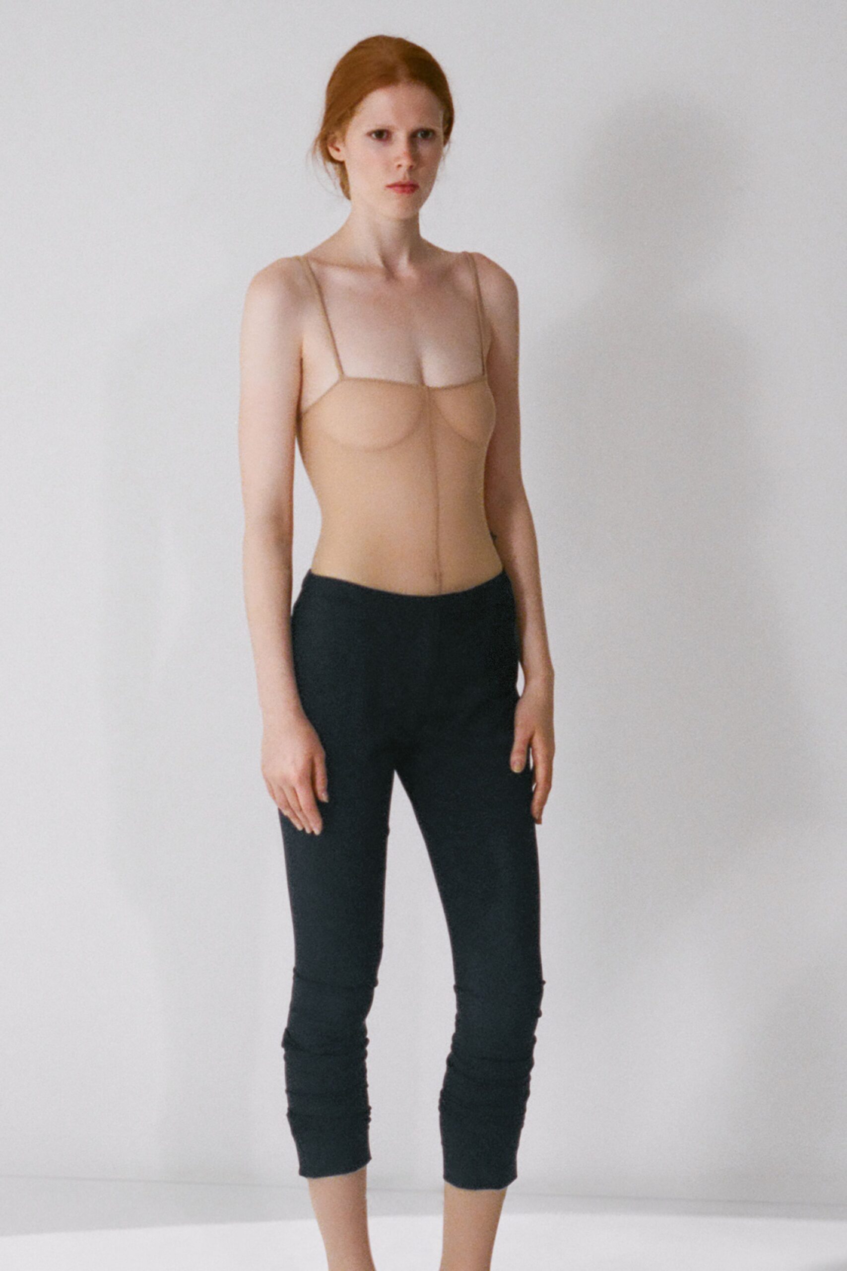 Nude stretch bodysuit with underbust seaming and a center front join. Black jersey capris, ruched tightly above the ankles. In a bare rental apartment before the mattress gets delivered.