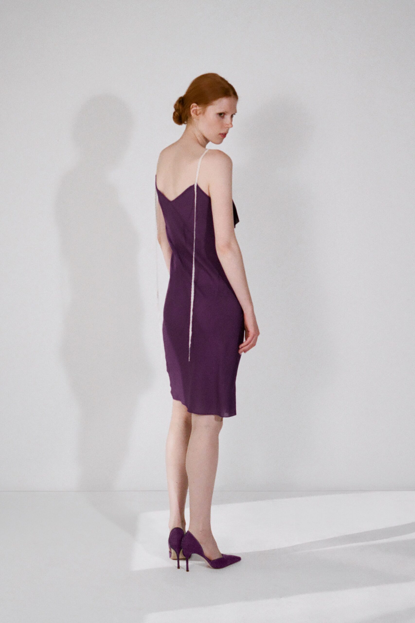 Deep aubergine slip dress, cut close with a V back and one cord strap hanging loose. Matching suede pumps with slim black stiletto heels. After the wedding, carrying your shoes across the hotel corridor ice machine glow.