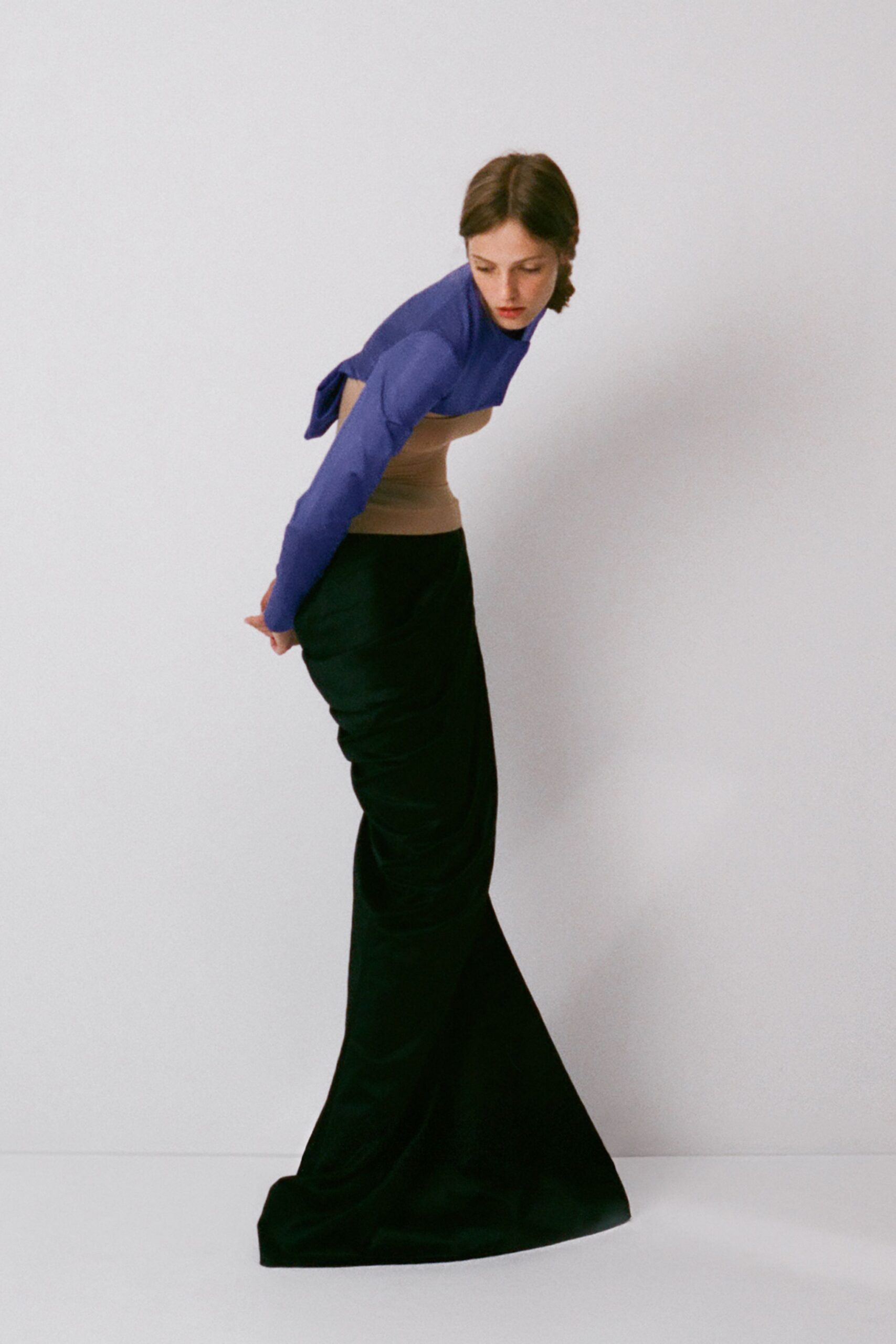 Periwinkle stretch-knit top with a high neck and open tied back. Nude ribbed band hugging the midriff like a built-in layer. Black floor-length skirt, ruched close through the hips before flaring. Waiting for the kettle in a rental with cold wooden floors.