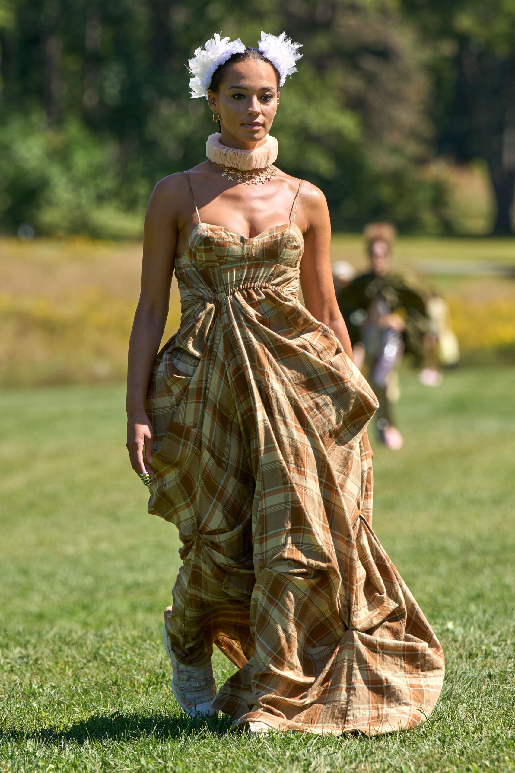 Two white tulle pompons perched over the ears. Peach pleated organza standing stiff around the neck. Tan plaid dress, bustier-seamed and ruched into a dropped waist swirl. Pale trainers half hidden by the dragging hem. Crossing the lawn after the wedding, heels abandoned somewhere near the tent.