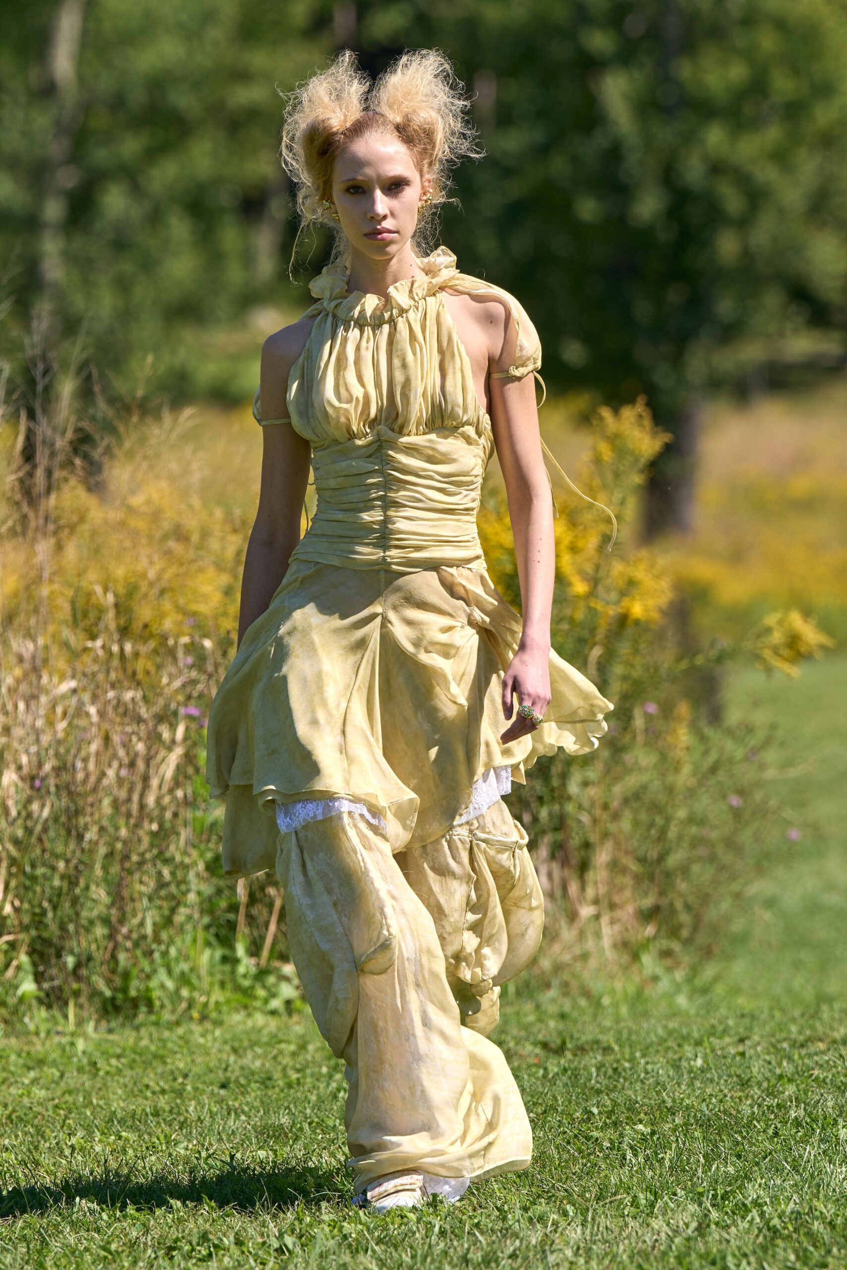 Buttercream satin dress with ruched bodice, ruffled halter and handkerchief overskirt. Matching loose trousers, gathered into bulbous knee puffs under the skirt. White shoes peeking from the pooling hem. Crossing a meadow after the garden wedding has thinned to family.
