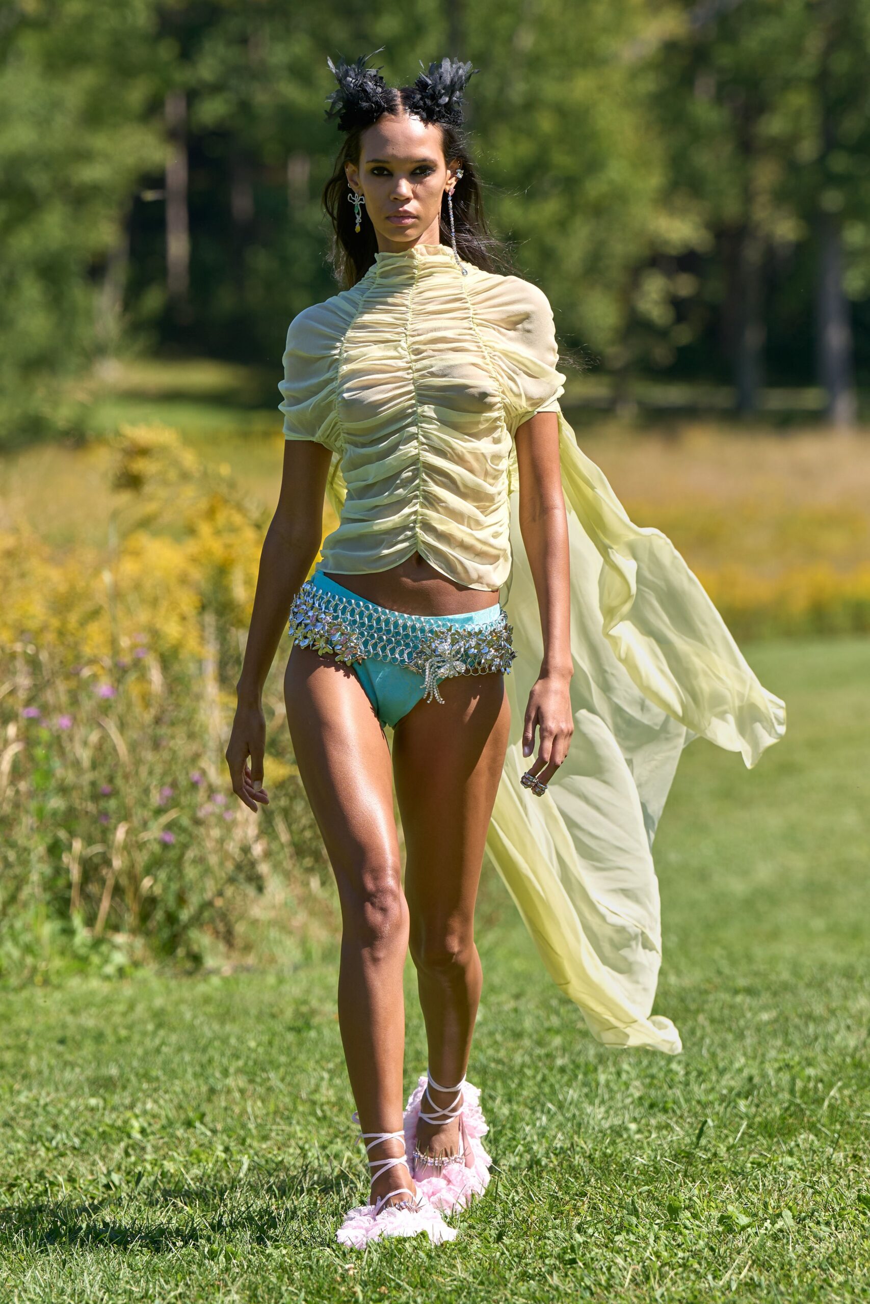 Buttercream chiffon top densely ruched up the center, one train streaming behind. Aqua briefs with a crystal chain fringe and starburst hip cluster. Mismatched crystal drop earrings. Lace-up sandals with pink marabou footbeds. Crossing a meadow after the wedding, shoes wet through with dew.
