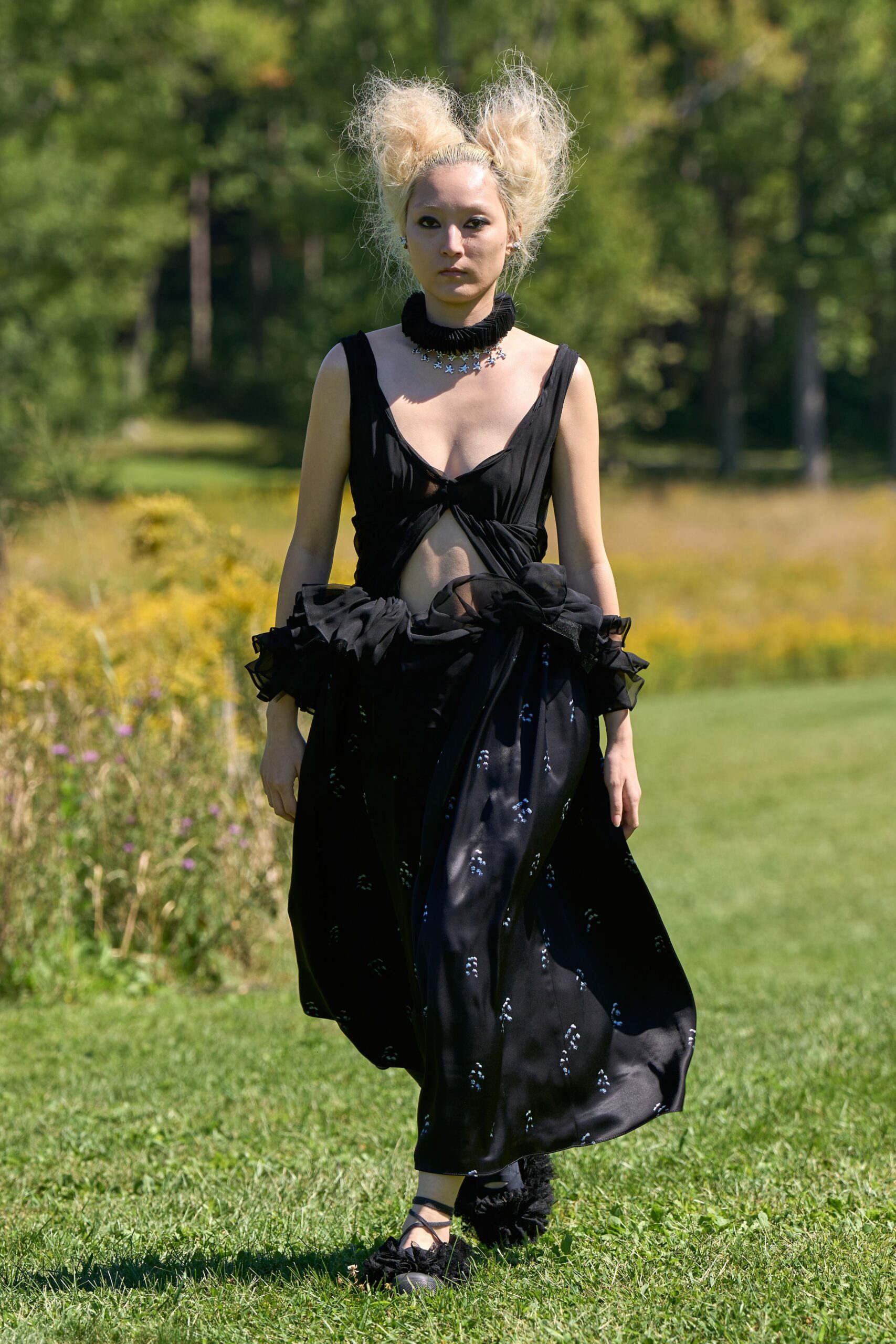 Black pleated ruff choker stacked over a ring of tiny stars. Black silk dress knotted under the bust, with organza ruffles pooling at the hips. Black leggings disappearing into fluffy ankle cuffs. Crisscross ballet flats with shredded rosettes at the toe. Crossing a meadow after the picnic turned strange.
