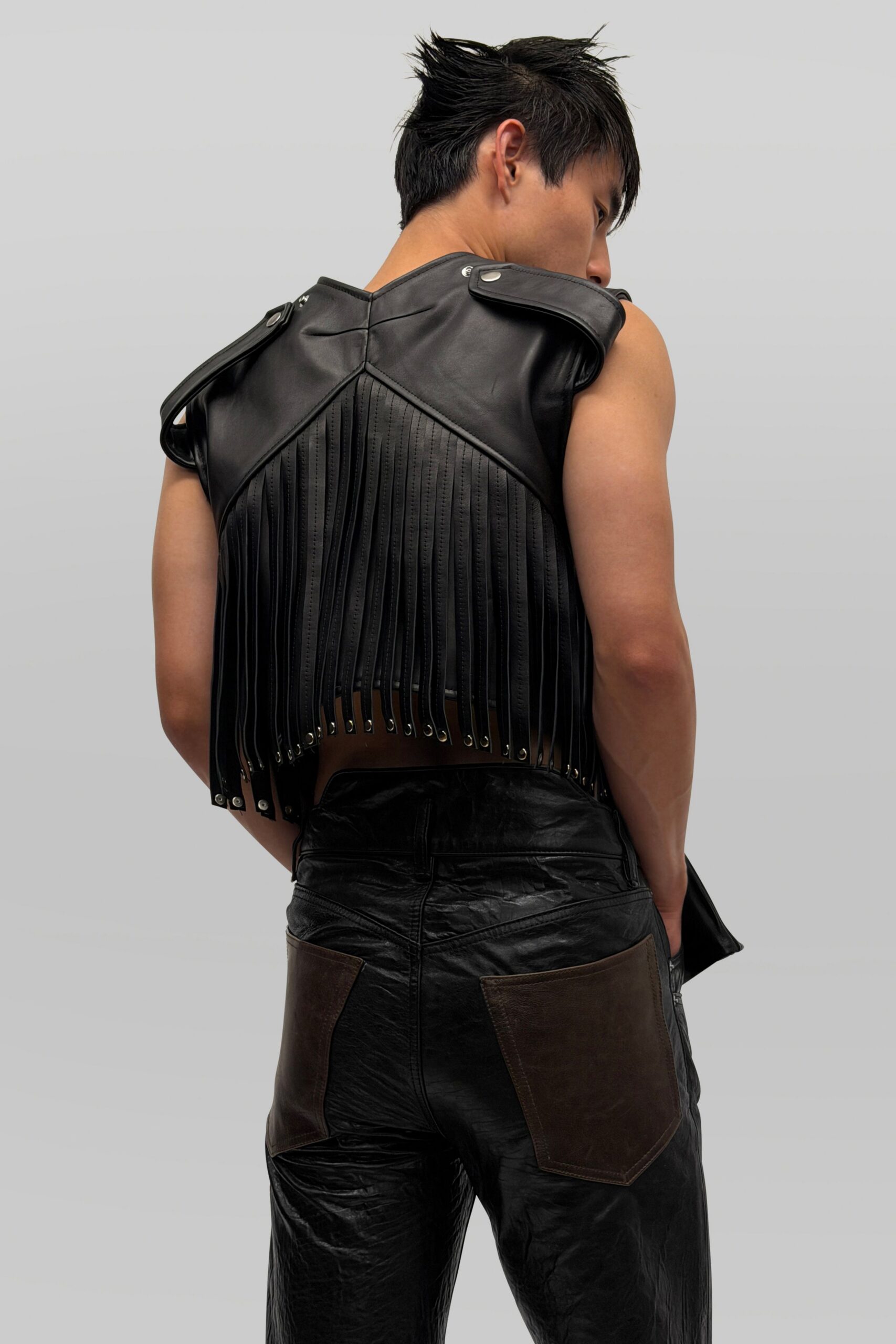 Black leather top with epaulets and a curtain of narrow back fringe. Crinkled black leather trousers, oversized brown patch pockets low on the seat. For crossing a fairground after dark with metal dust on your hands.