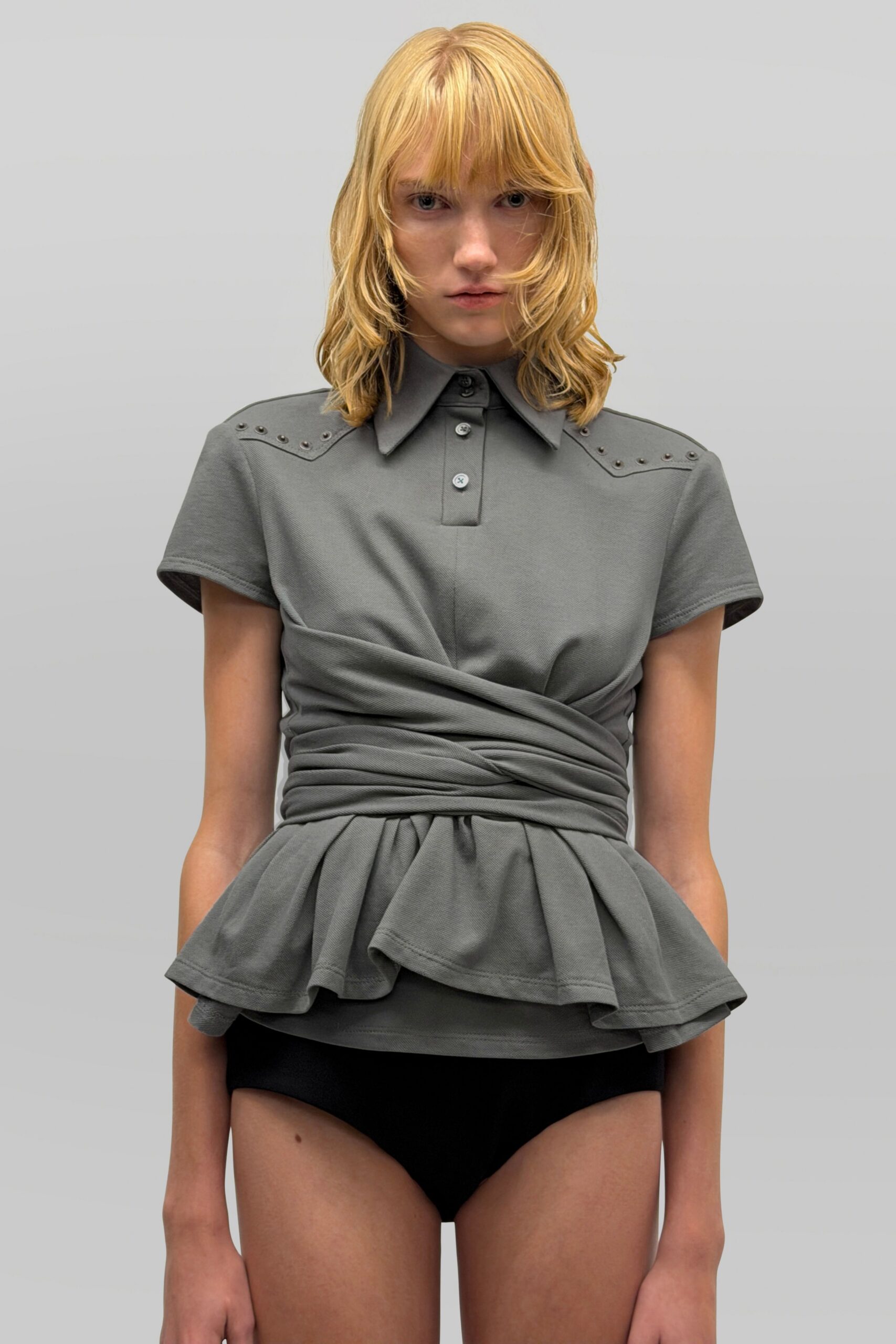 Slate piqué polo top with metal studs tracing the shoulder yokes. Same fabric wound tightly around the middle, ending in a peplum flare. Black jersey briefs cut high on the hip. For the overheated hour before dinner at a golf resort.