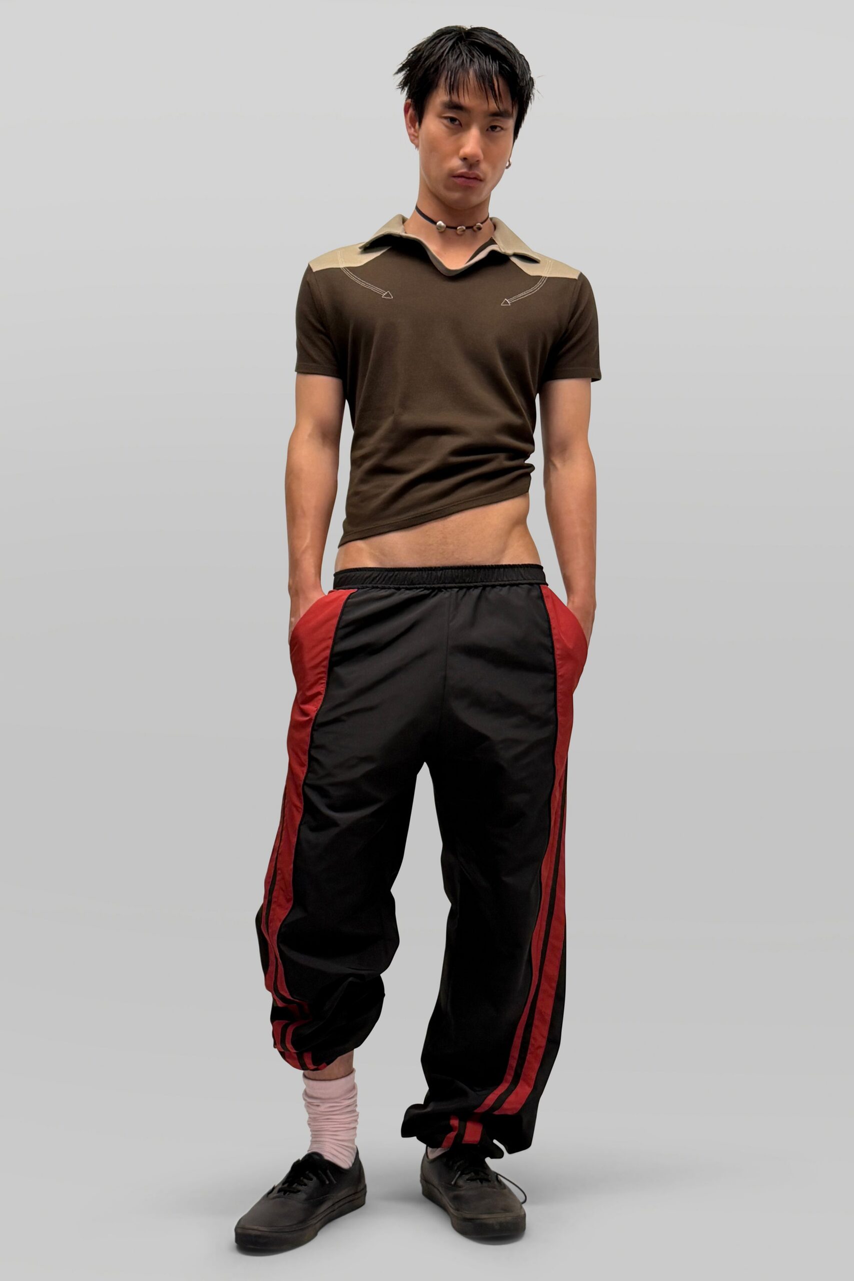 Chocolate stretch polo with beige yoke and curved contrast topstitching. Pearl choker with tiny shell-like spacers. Black nylon track pants, red side panels and pooled cuffs. Pale pink slouch socks. Black skate shoes, one lace dragging. Walking out of the corner store with a sports drink after midnight.