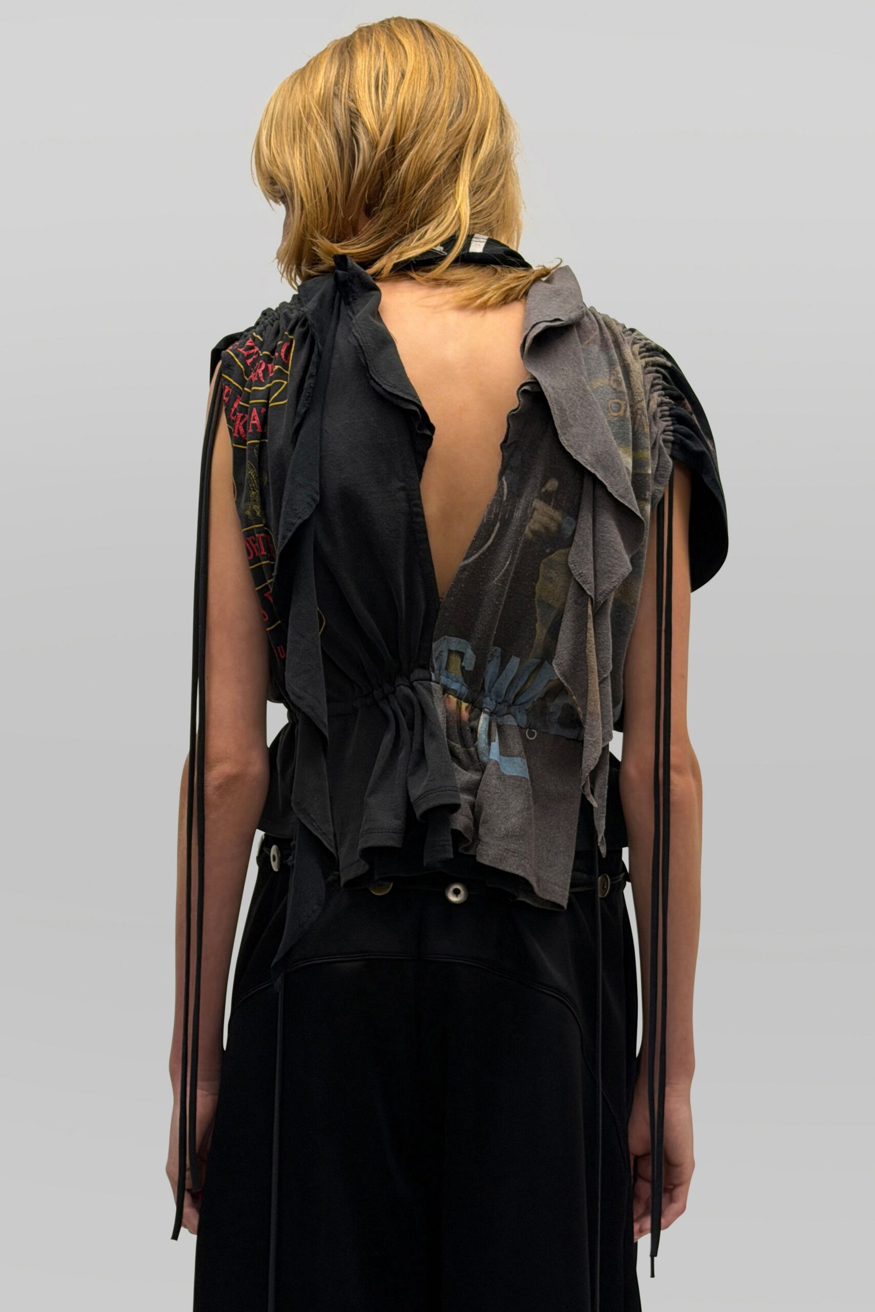 Spliced black and charcoal jersey top, ruched shoulders and a plunging open back. Long black cords hanging straight past the elbows. Black wide-leg trousers with white grommets circling the low waistband. For crossing an empty fairground after the generators cut out.