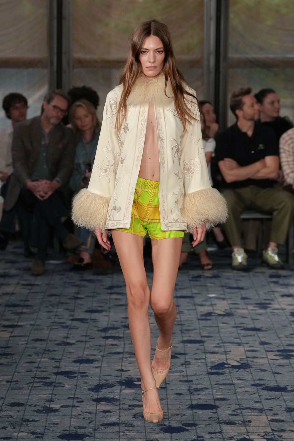 Ivory satin cape, tone-on-tone floral embroidery with shaggy cuffs and collar. Neon citron pleated shorts, striped panels and a gathered waistband. Nude patent pumps with a fine ankle strap. For crossing a hotel atrium after noon, still dressed for dawn.