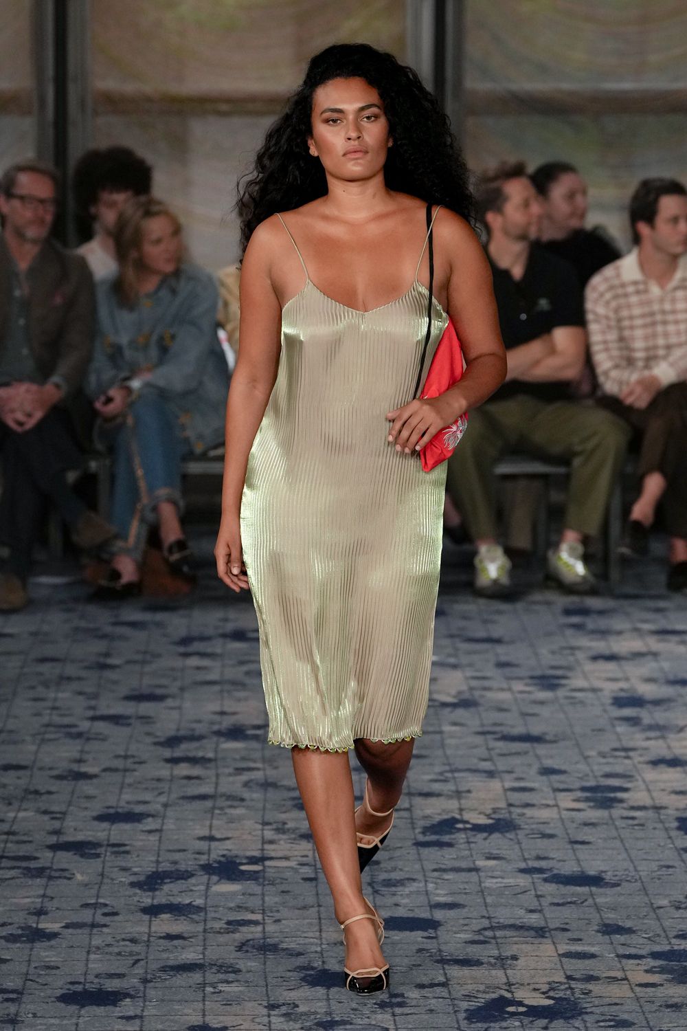 Pale pistachio plisse slip dress, narrow straps and a tiny lettuce hem. Coral satin shoulder bag tucked tight under the arm. Cream slingbacks with glossy black cap toes and fine straps. Crossing a tiled hotel courtyard just before the pool lights switch on.