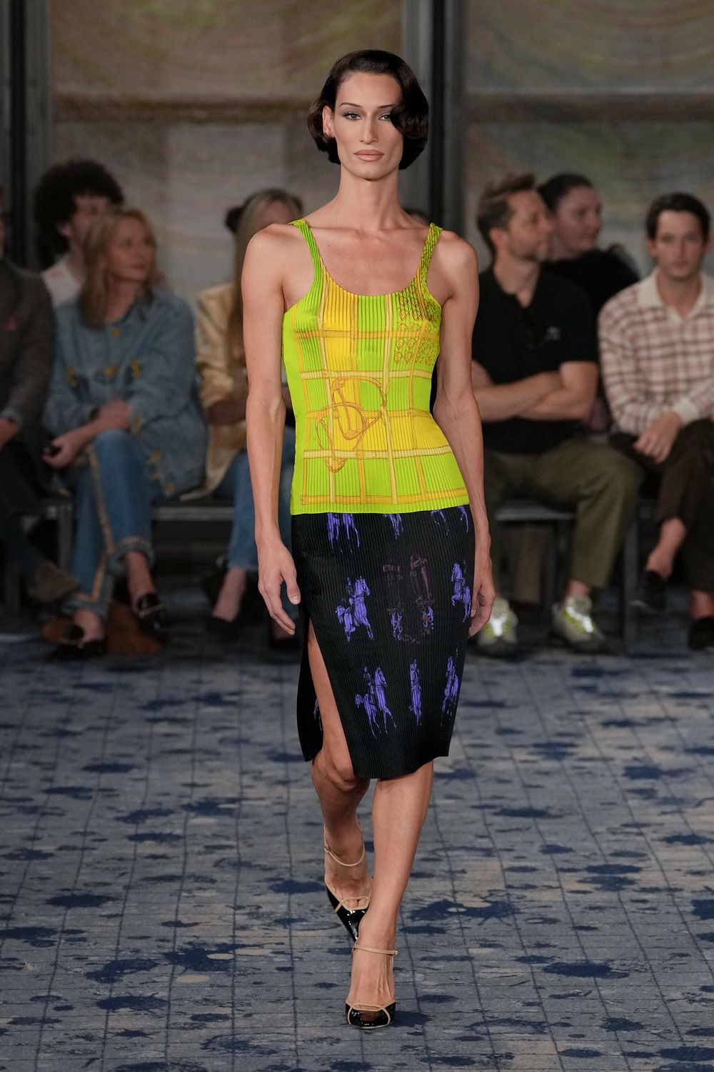 Acid-lime ribbed knit tank, chart lines traced in ochre cord. Black ribbed midi skirt with violet horse figures and a thigh slit. Black patent cap-toe slingbacks with thin nude straps. Walking across a racecourse terrace after the last bet is lost.