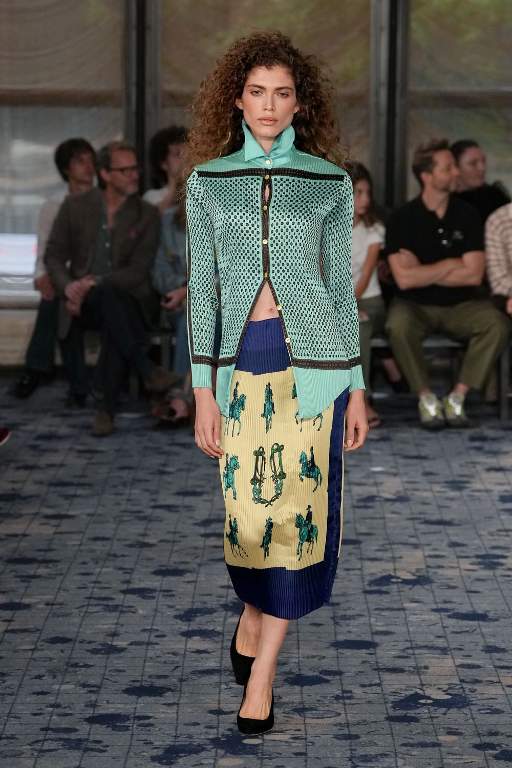 Mint open-knit cardigan, black laddered trim and a high stand collar. Ribbed cream midi with teal horse motifs and a navy side panel. Black suede pumps. Walking across a tiled courtyard after the riding lesson emptied out.