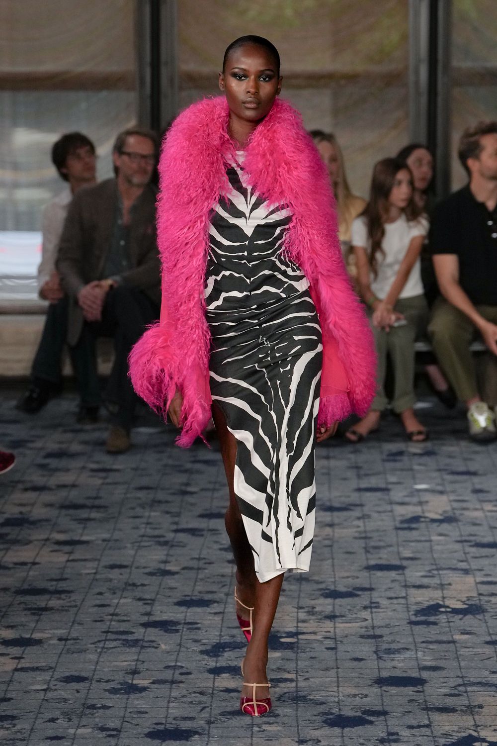 Hot-pink shaggy fur stole, sleeves swallowed in the long pile. Black-and-white zebra slip dress, ruched through the hips with a thigh slit. Fuchsia toe-cap sandals with clear straps. Hotel lobby carpet after midnight, still carrying heat from the street.