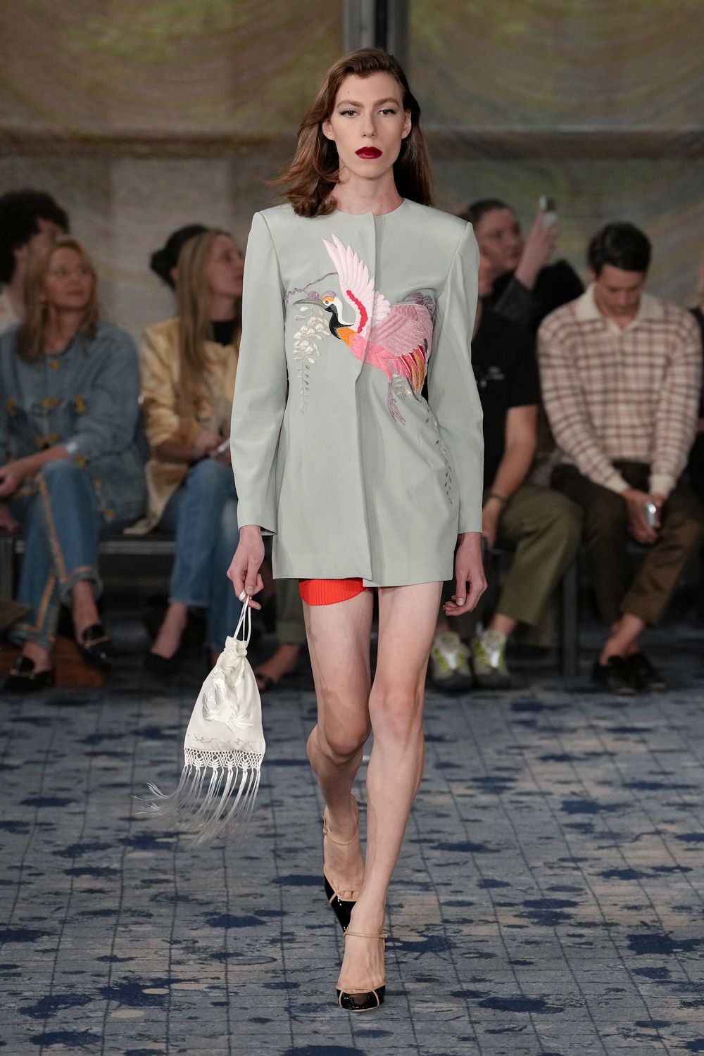Pale celadon jacket dress with a crane appliqued across the chest. Ribbed orange knit shorts peeking below the split front. Ivory satin pouch with lace inset and long fringe. Black patent cap toes on nude slingback straps. For a garden party that somehow ends with shoes in your hand.