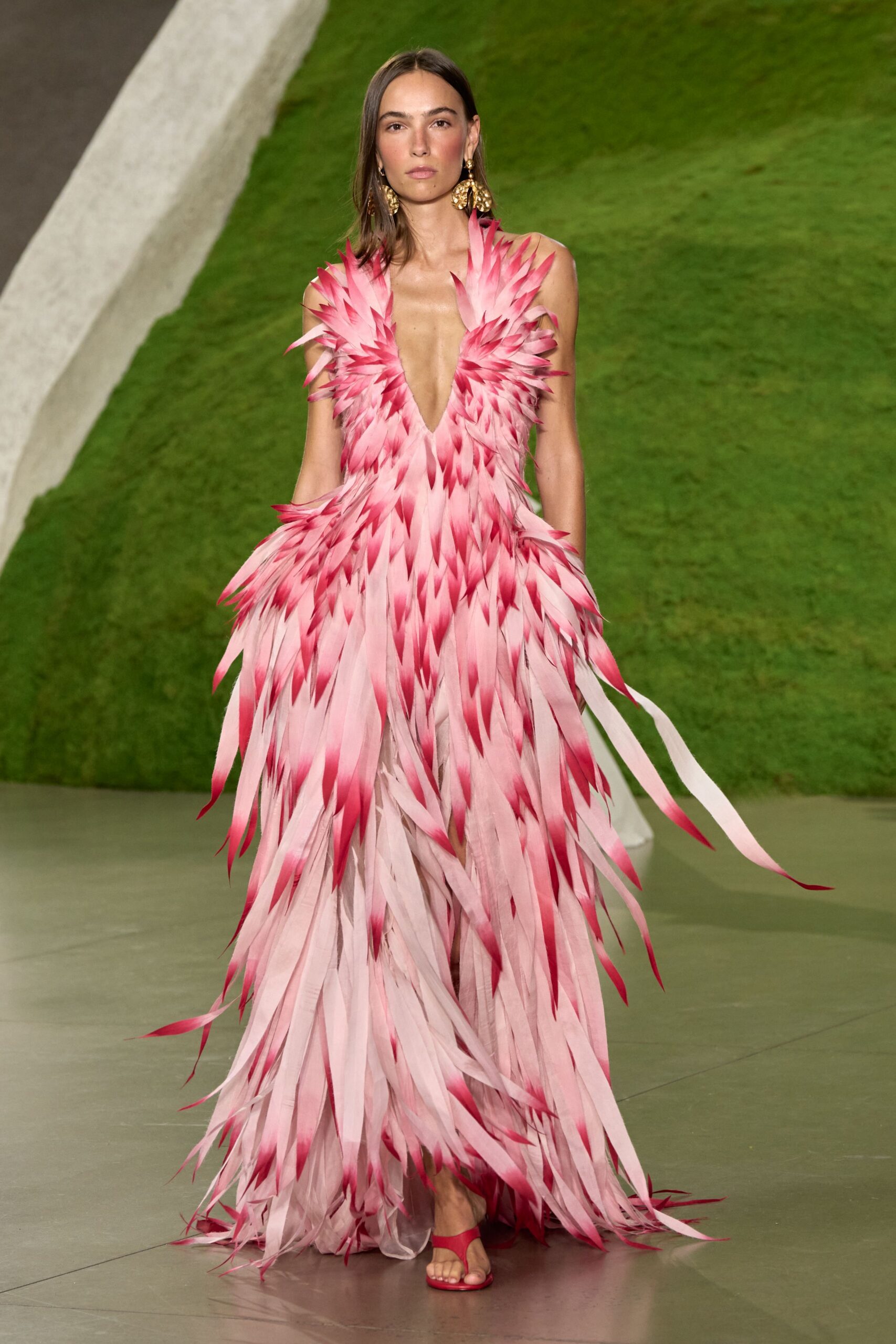 Blush plunge gown covered in long petal strips, airbrushed crimson at the tips. Oversized gold shell drops. Flat red thong sandals. Crossing a hotel lawn after midnight with flower garlands coming undone.