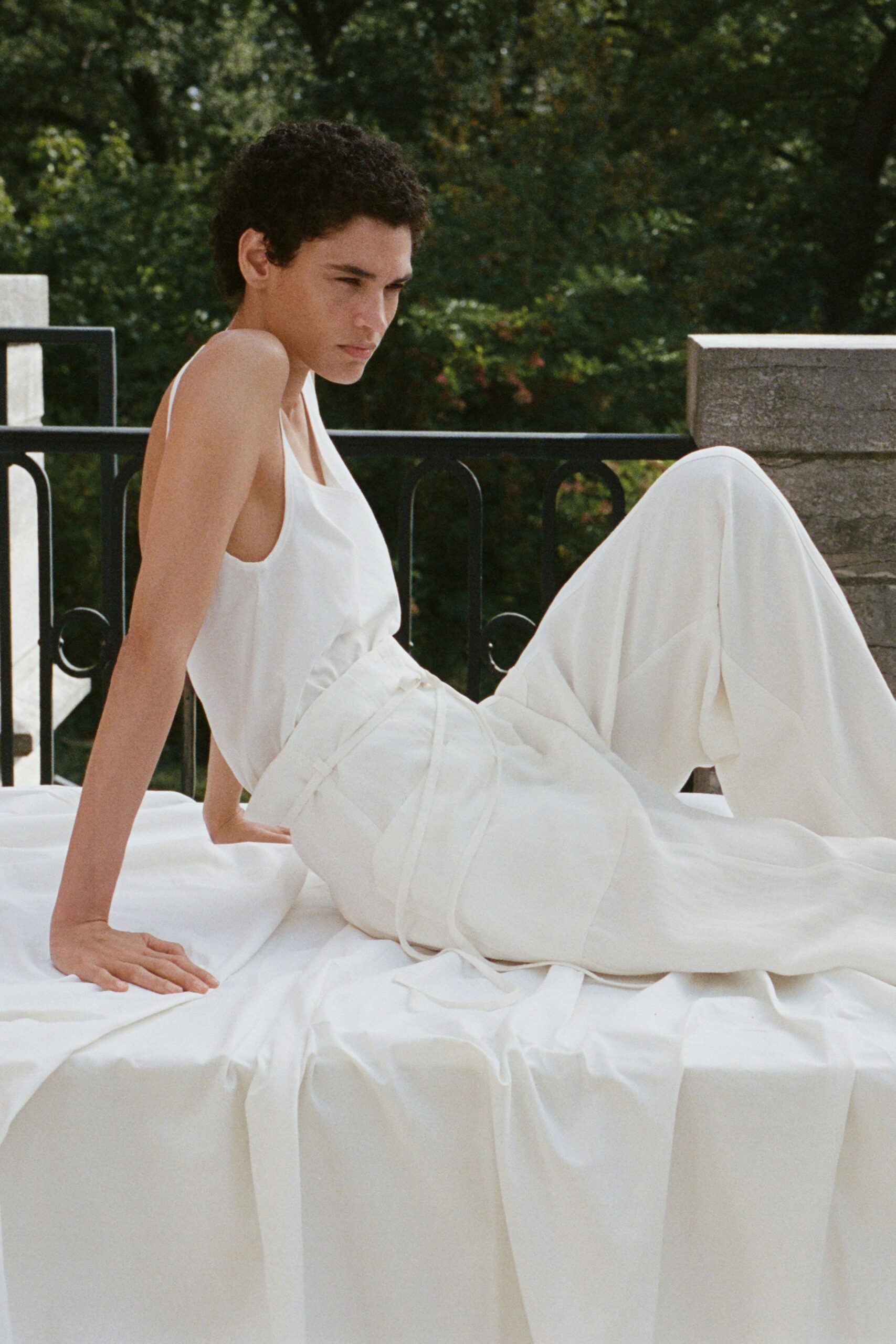 Ivory fluid tank with a scooped neck and deep armholes. High-waisted ivory wide-legs, wrapped with self ties trailing over the sheet. Terrace heat before noon, the stone still cool against your back.