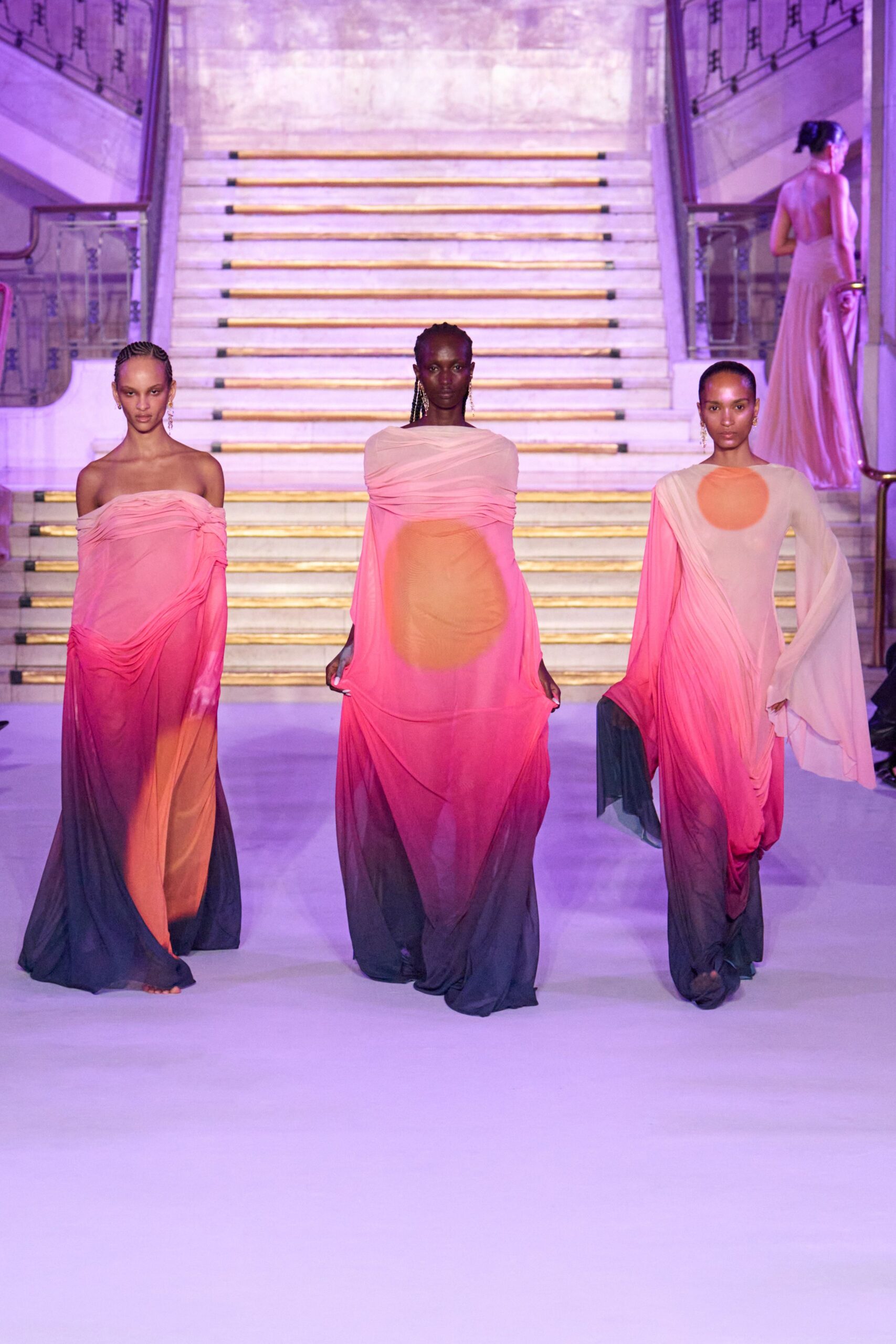 Sheer draped column dress in blush, fuchsia and slate ombre, gauze wrapped across the shoulders. Descending a marble staircase while the ballroom lights turn lilac.