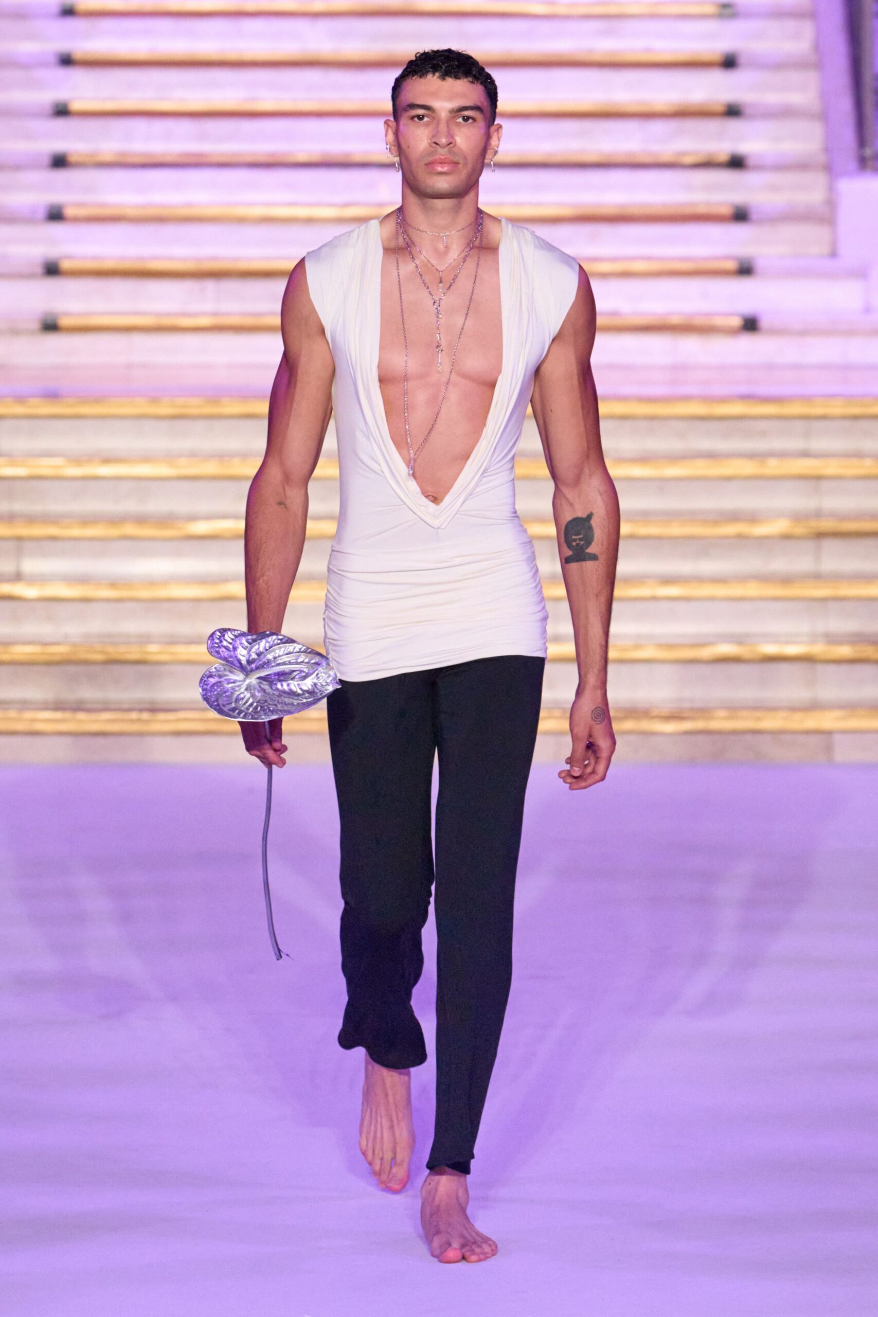 White jersey top cut to a plunging cowl, ruched through the waist. Layered silver chains dropping nearly to the navel. Black skinny trousers with split hems breaking over bare feet. Metallic lavender inflatable flower on a long trailing stem. Walking out of a bathhouse into violet dawn with party flowers left over.