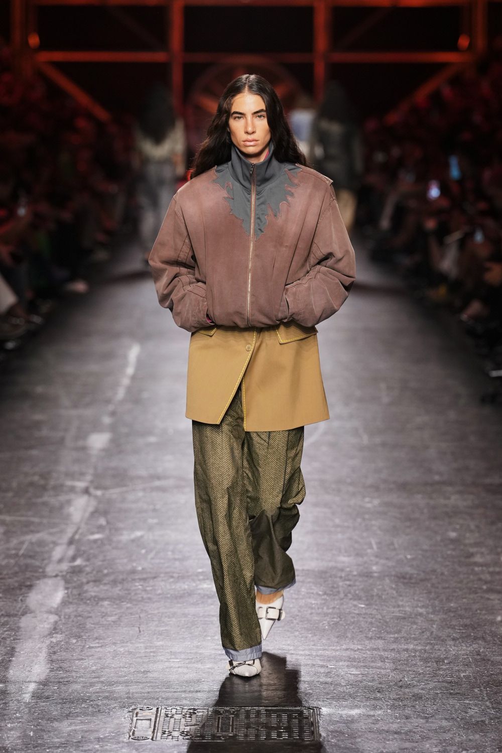 Dusty mauve suede bomber with a dark scalloped inset at the zip. Ochre wrap mini with thick topstitching and one off-center button. Olive herringbone trousers pooling long over turned pale cuffs. White pointed heels with oversized silver buckles. Walking across the fairgrounds after rain, clutch ticket already damp.