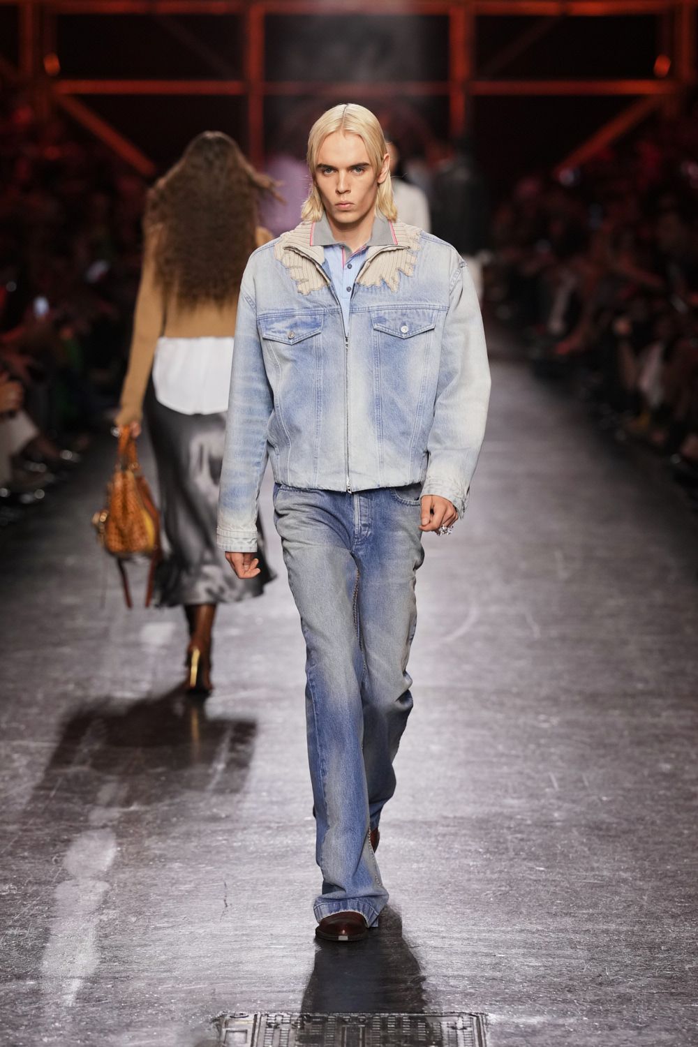 Bleached blue denim jacket with ribbed knit yoke peeling at the shoulders. Powder-blue polo, pink piping tracing the collar edge. Faded straight-leg jeans pooling lightly over the shoe. Dark leather square toes. Walking the boardwalk before noon, sea mist still on the railings.