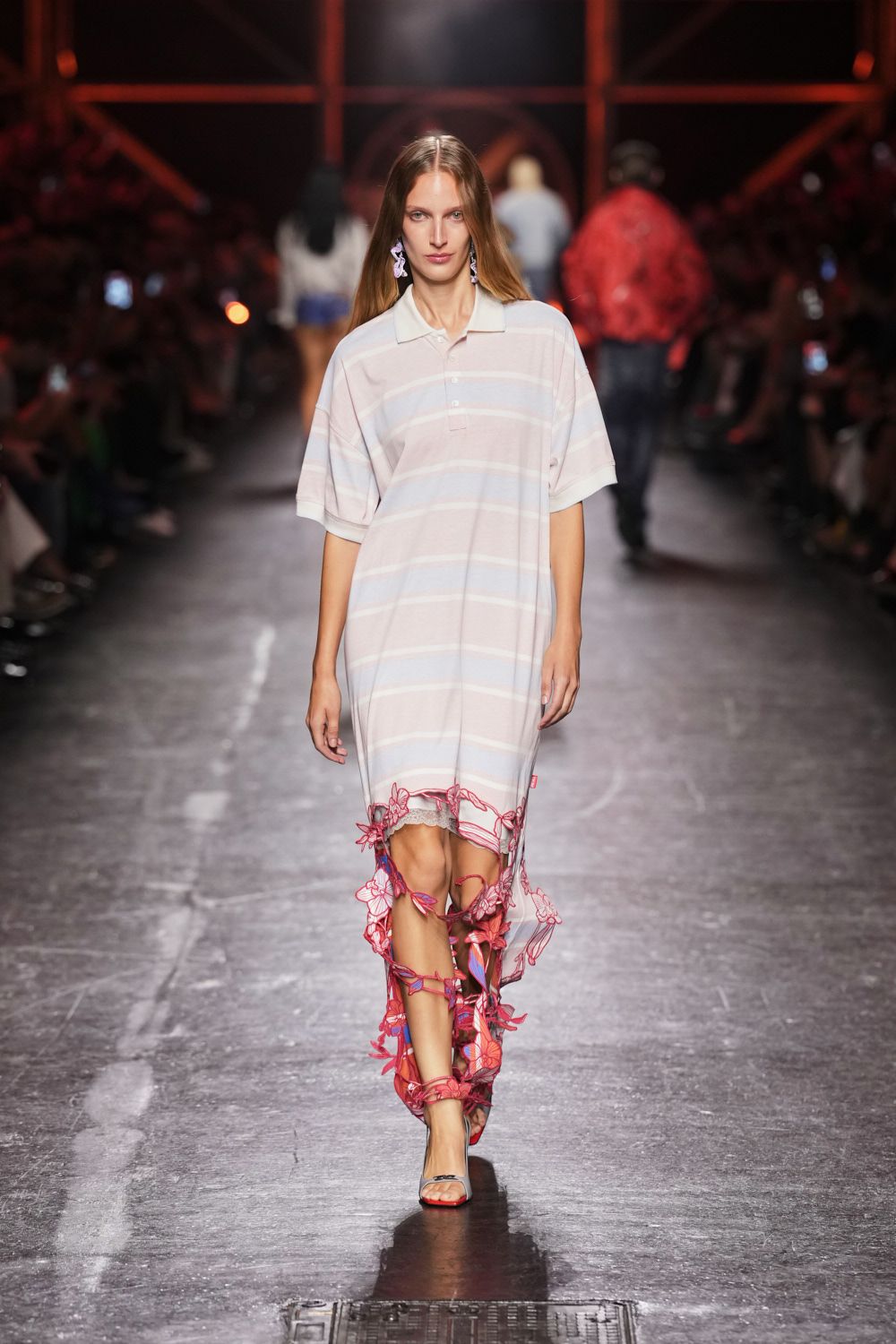 Oversized blush knit polo dress with faint horizontal stripes and dropped shoulders. White lace slip peeking from the shredded hem. Pink mesh floral appliques twining from calf to ankle in loose strips. Clear-strap heeled sandals. Walking home from a beach wedding with seaweed still stuck to your feet.