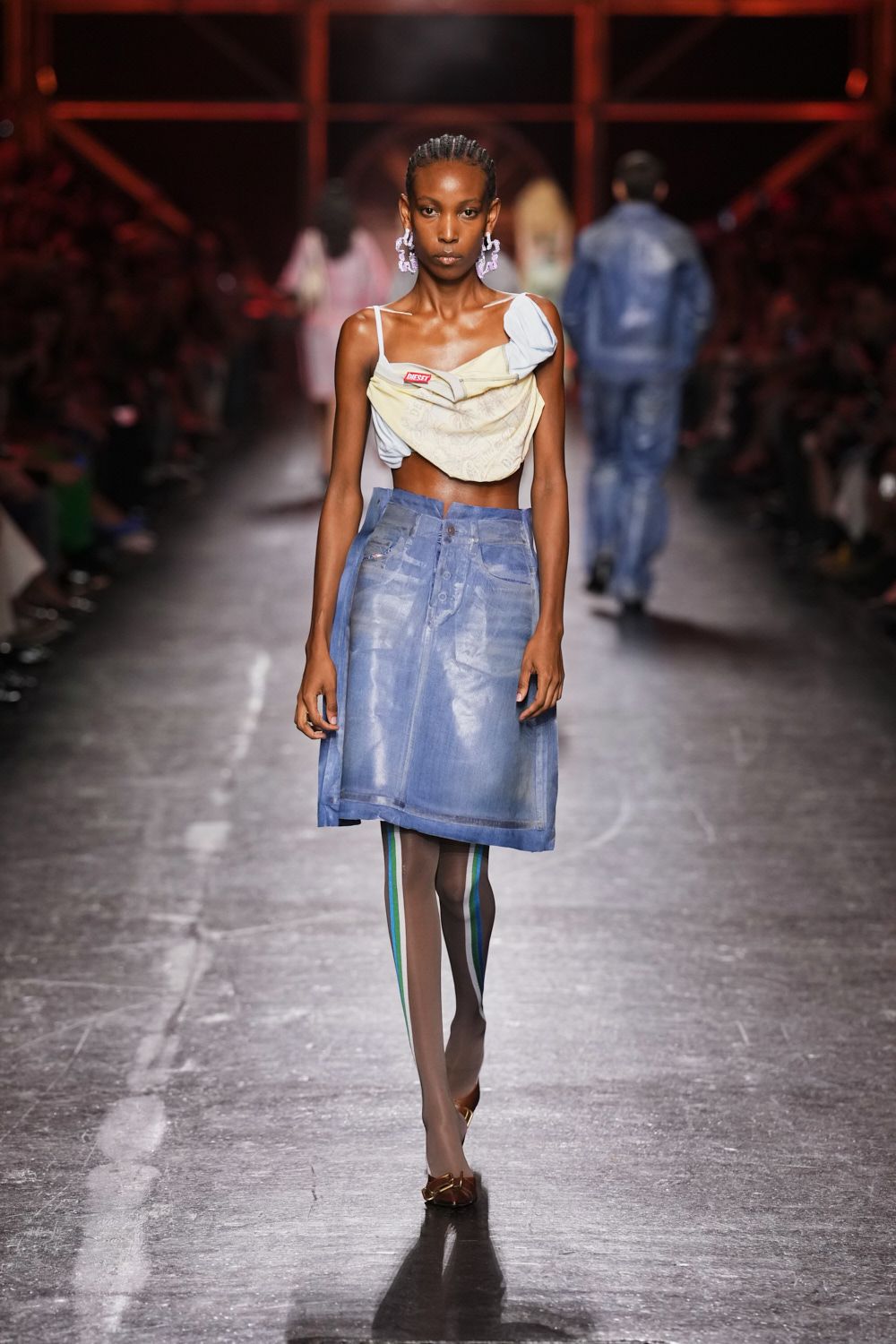 Pale lilac dangling figures at both ears. Asymmetric draped cream scarf top, one strap slipping off the shoulder. Powder-blue coated denim A-line skirt with a raw front seam. Sheer taupe tights with teal and indigo side stripes. Bronze flats with a knotted bow. Walking to the corner shop in summer with last night's shirt retied.