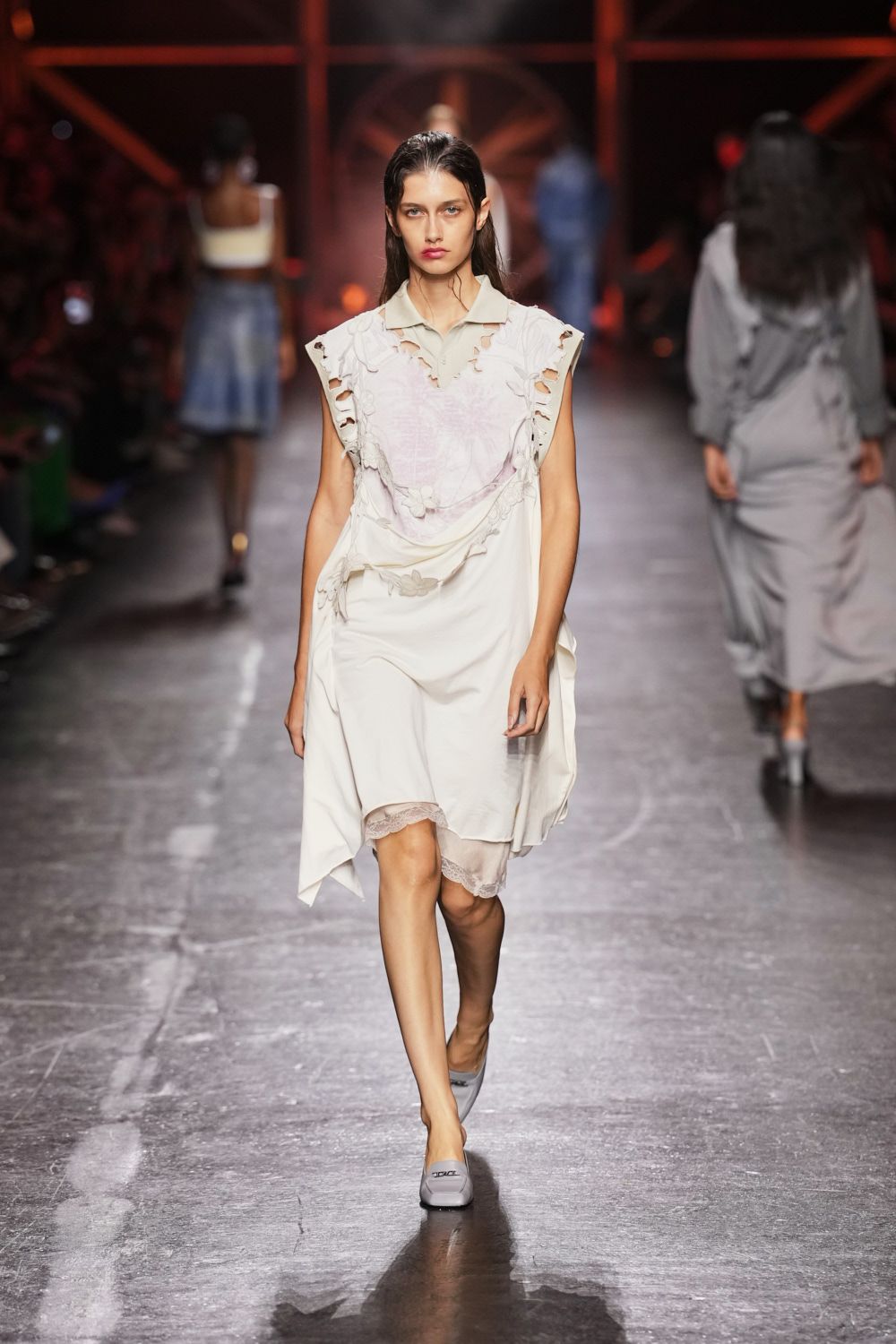 Cream slip dress draped with torn petal-edged overlays and a pale polo collar. Blush underlayer peeking in lace at the uneven hem. Pale grey square-toe flats. Morning after the wedding, carrying shoes across a damp hotel lawn.