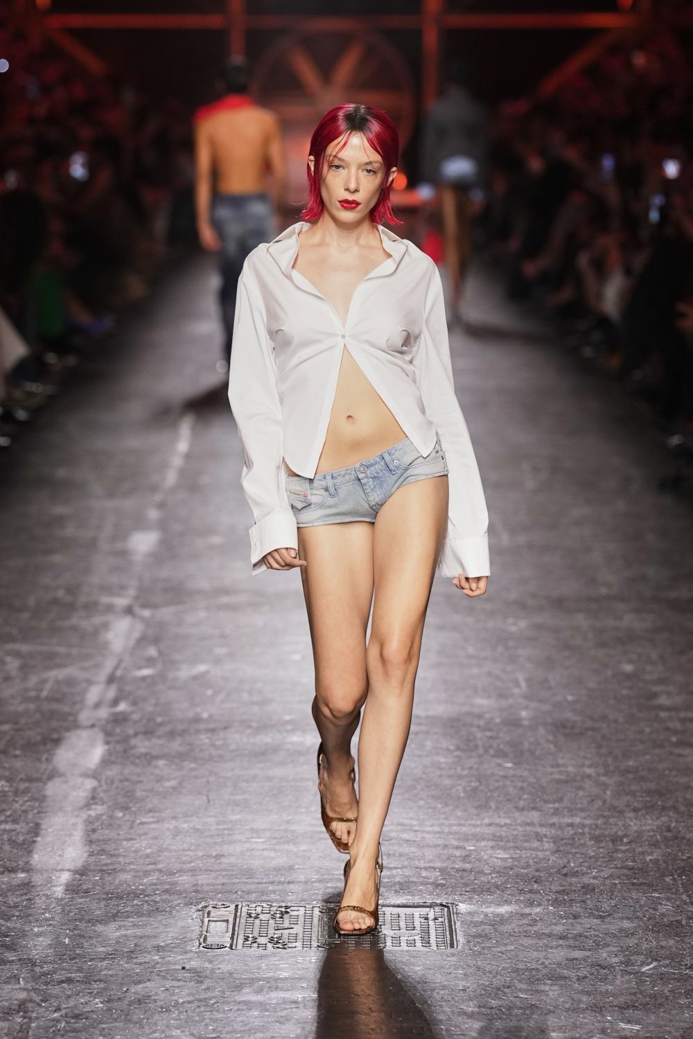 White stretch shirt pinched to a single button under the bust. Pale stonewashed denim hot pants, waistband dipped low on the hip. Barely-there tan ankle-strap sandals. Walking back from the motel ice machine at sunrise.
