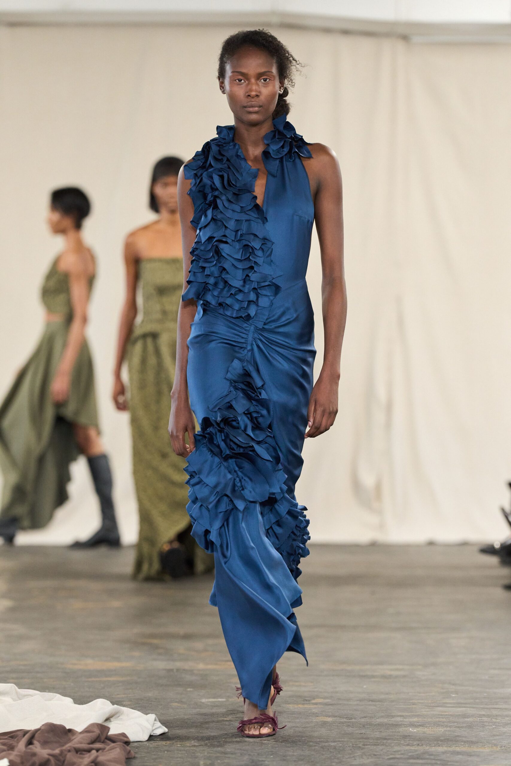 Cobalt satin gown with a plunging slit and cascades of raw-edged ruffles. Wine satin sandals tied in frayed wisps across the toes. For arriving late to a terrace wedding with dust on the paving stones.