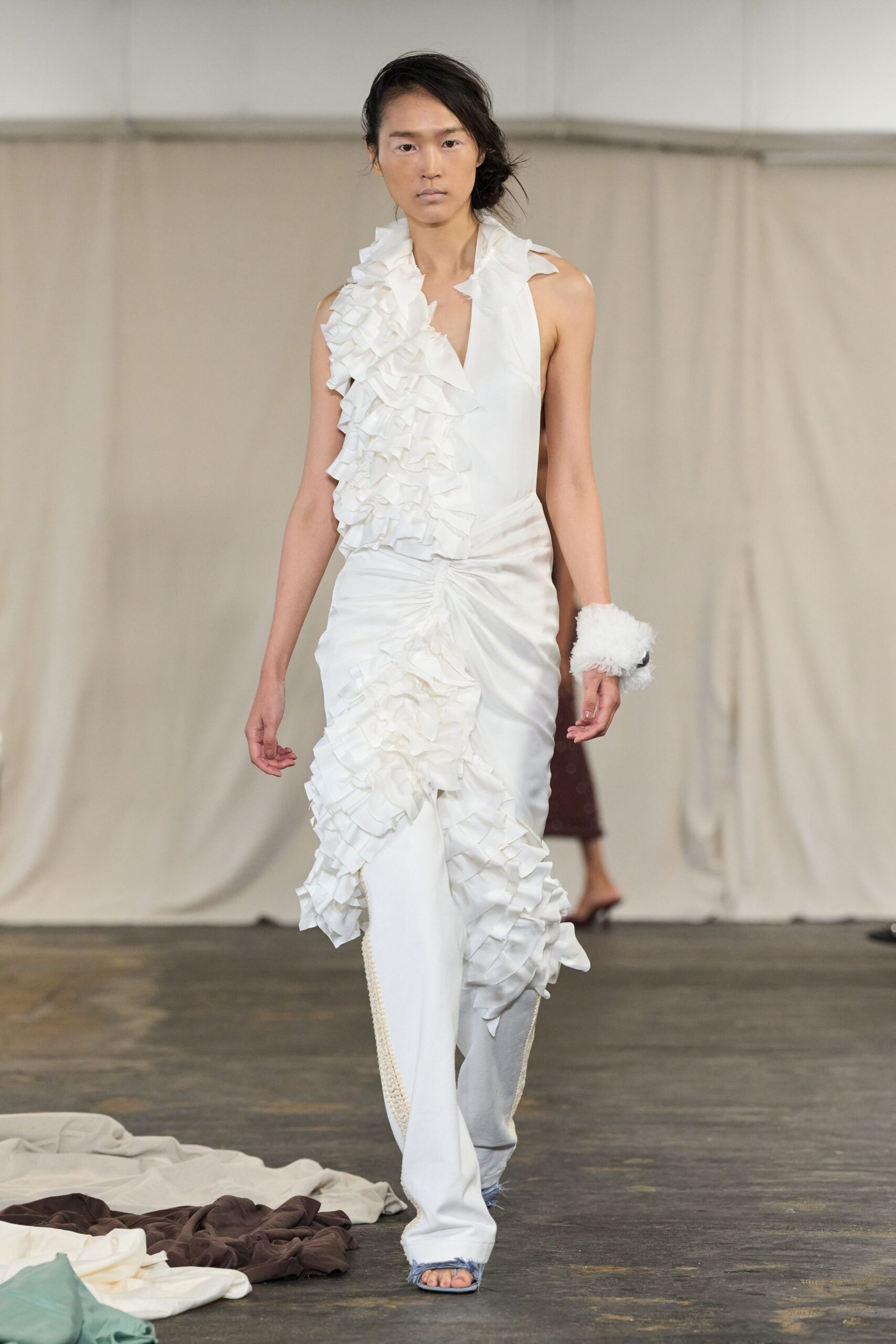 White satin top with a plunging V and dense cascade ruffles. White satin trousers ruched hard at the hip, ruffles spilling down one leg. Fluffy white wrist cuff. Pale blue toe-baring sandals with frayed denim at the front edge. For crossing a hotel ballroom after the wedding cake has collapsed.
