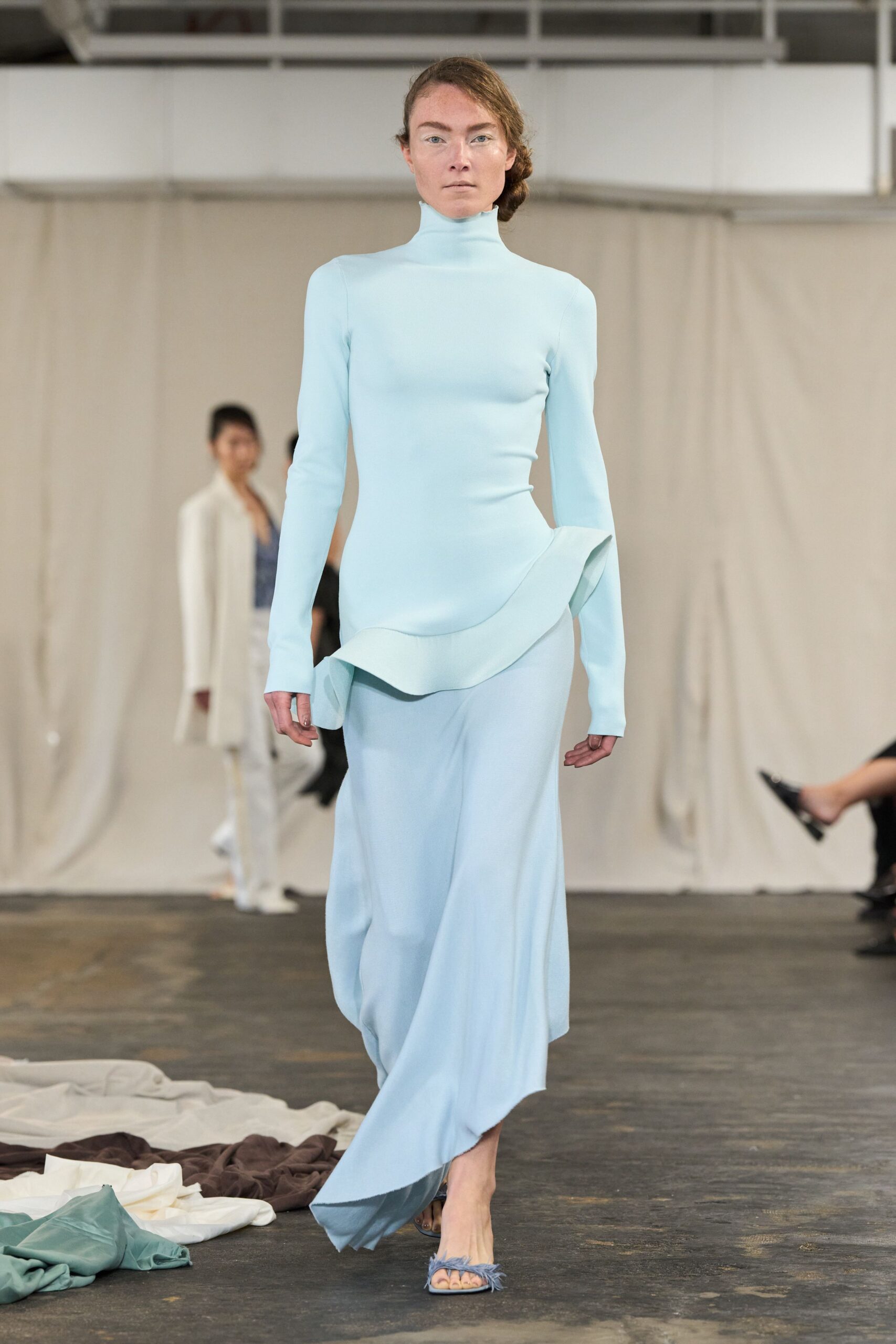 Powder-blue stretch dress with a high funnel neck and one fluted hip ruffle. Matching open-toe mules topped with wispy feather trim. Walking through a sculpture court before the fountains switch on.