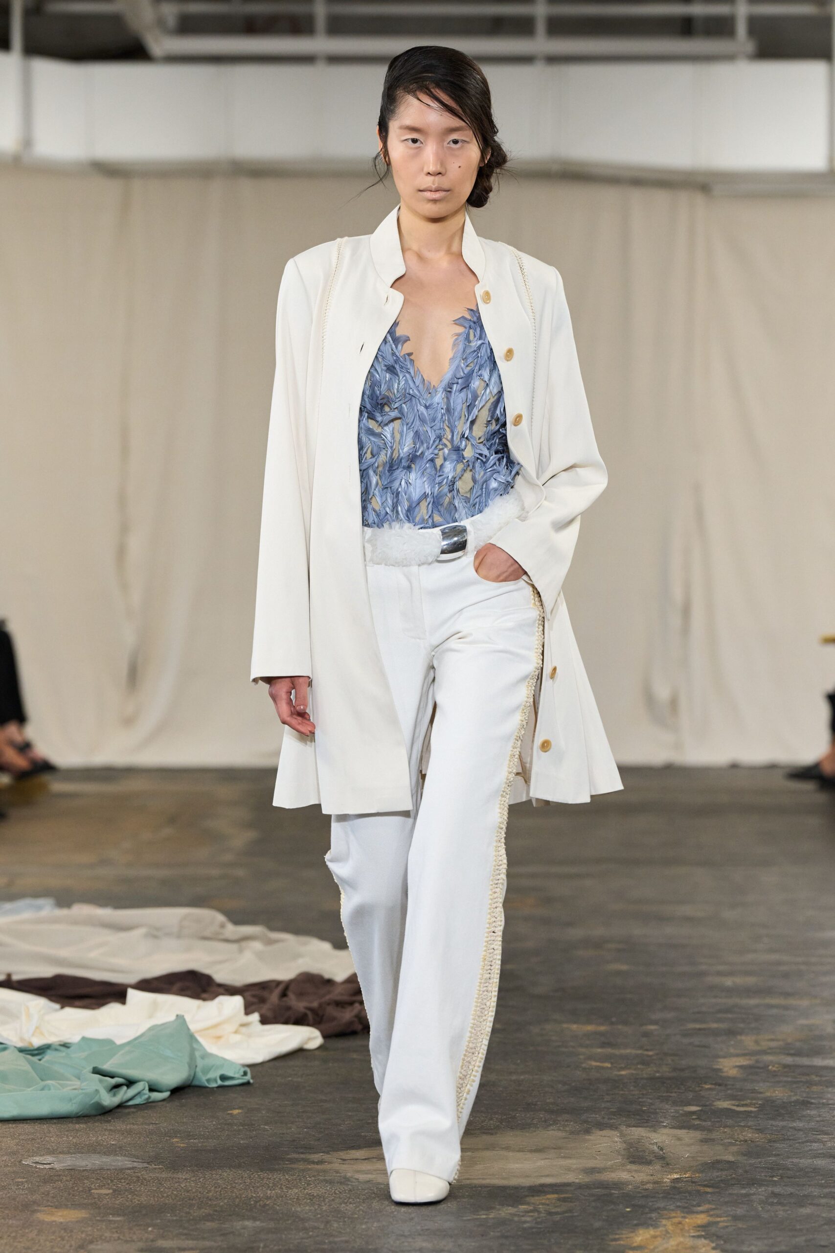 Ivory swing coat with bracelet seams and spaced horn buttons. Powder-blue feathered lace top, cut to a deep jagged V. White furry belt with a blunt silver plaque buckle. Ivory trousers trimmed with thick braided cord down the side seam. Square white boots. For walking through a sunlit atrium after leaving one earring behind.