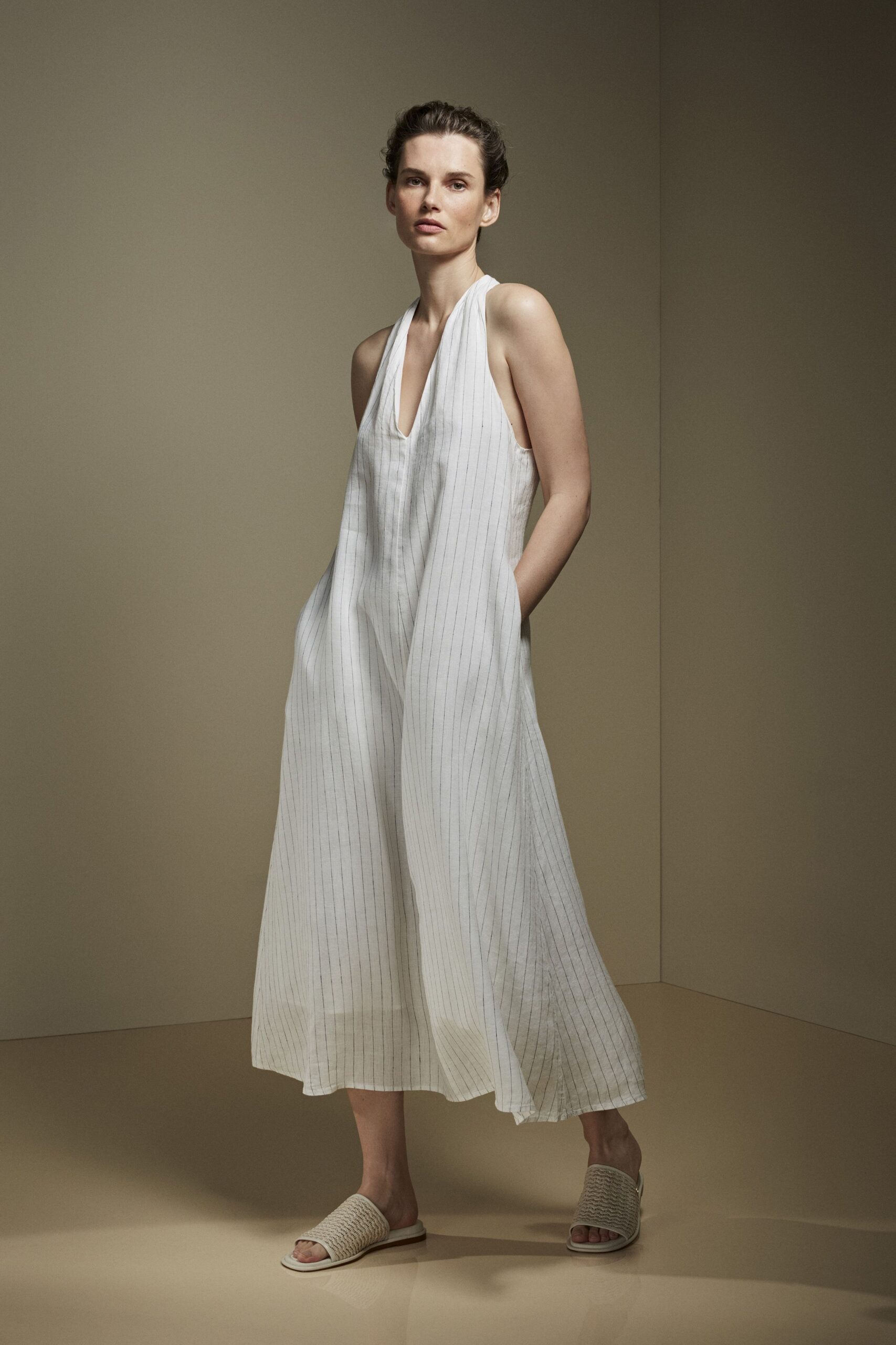 White pinstriped halter dress, plunge V and airy volume through the skirt. Cream woven slides with broad basket-textured straps. For the first hour awake in a rented house by the sea.