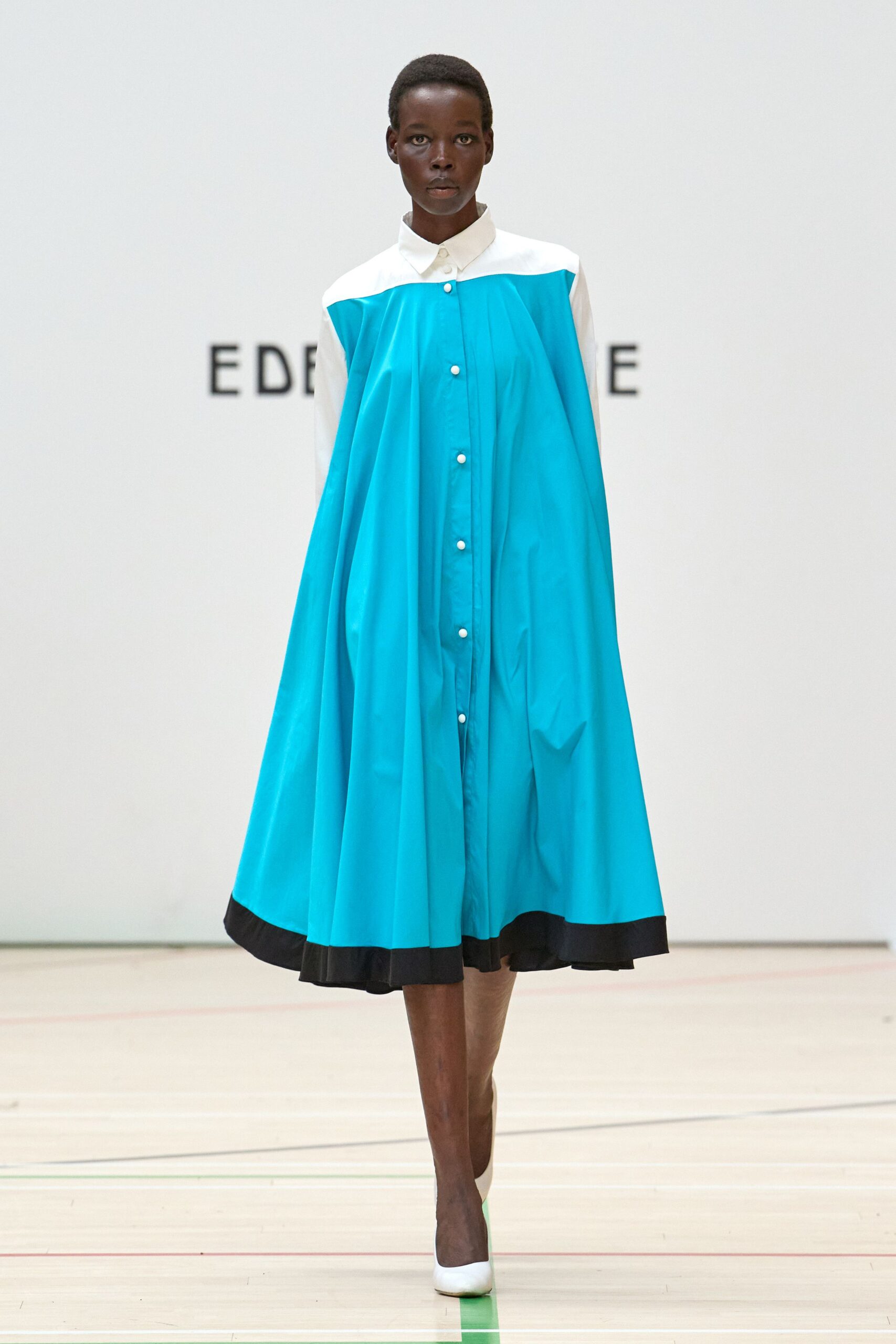 Turquoise shirt dress cut in sweeping tent volume, white yoke and black hem band. White pumps with a turquoise-tipped vamp. Crossing a school gym after hours, still hearing the squeak of the floor.
