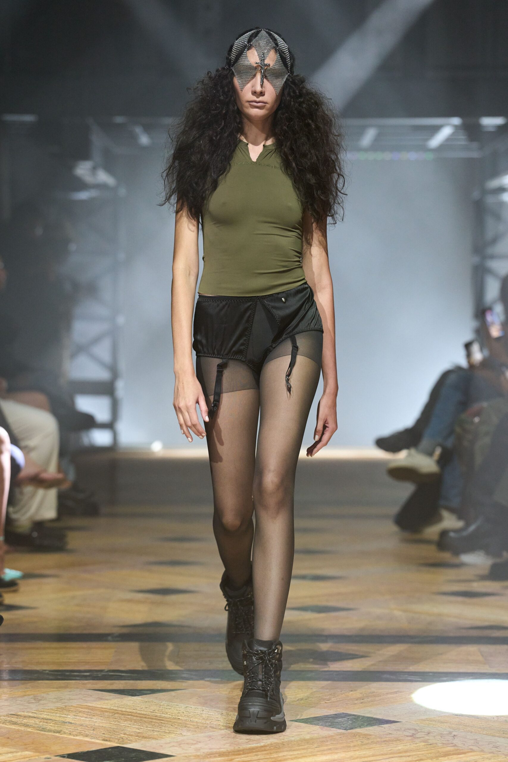 Chainmail insect mask with pointed eye flaps and a center clasp. Olive stretch jersey top, tightly ruched into the right waist. Black satin briefs with sheer front panel and dangling garter tabs. Smoke sheer tights. Black hiking boots, thick treaded sole. Walking across a gym floor after the costume trunk got raided first.